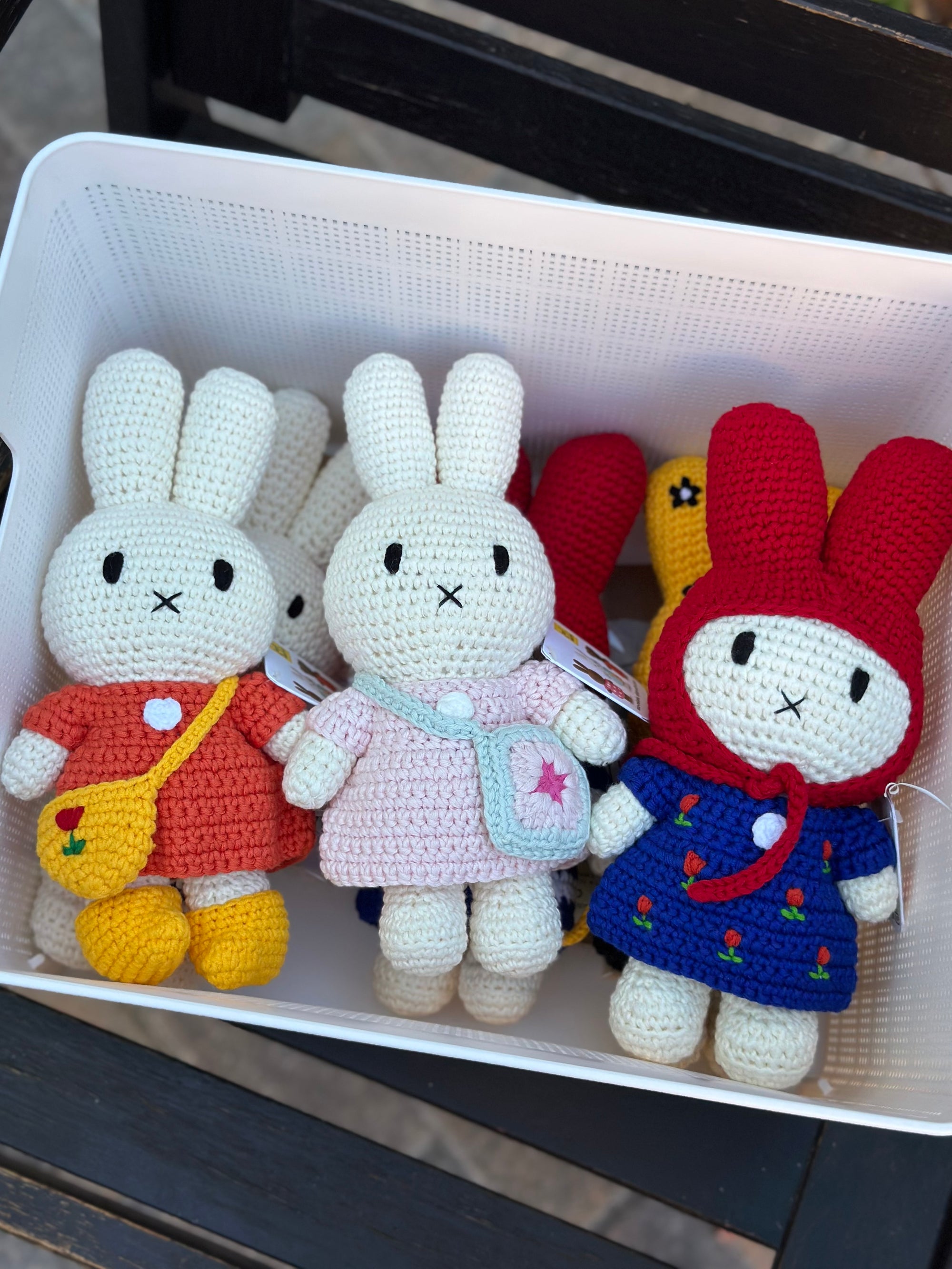 Handmade crochet Miffy plush in red dress with tulip bag, displayed in a basket with other crochet Miffy dolls in colorful outfits.