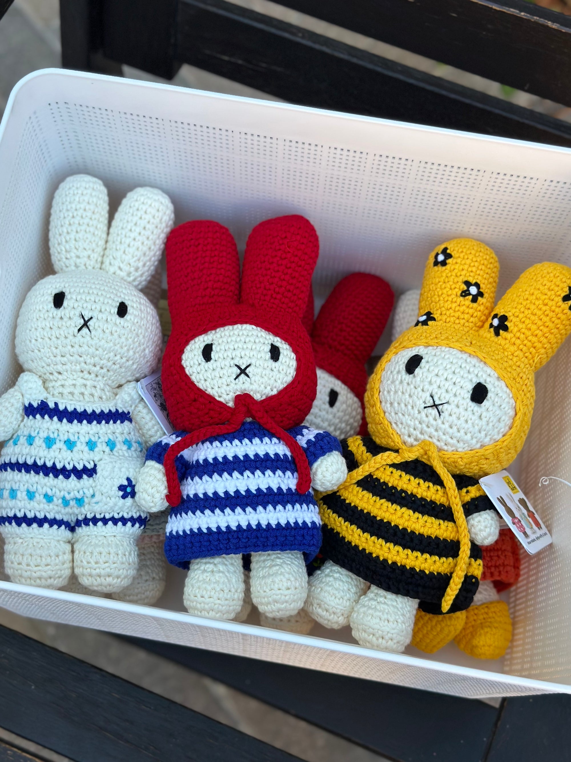 Basket of handmade Miffy crochet plush dolls, including a bee outfit Miffy with bonnet, surrounded by others in red and blue striped dresses.