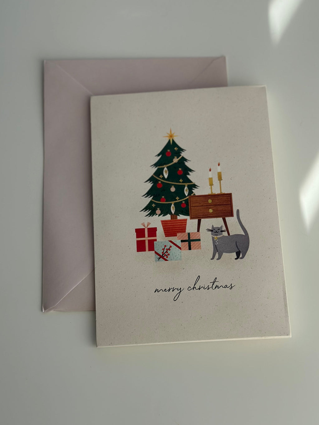Merry Christmas card with gray cat and tree shown with soft blush envelope.