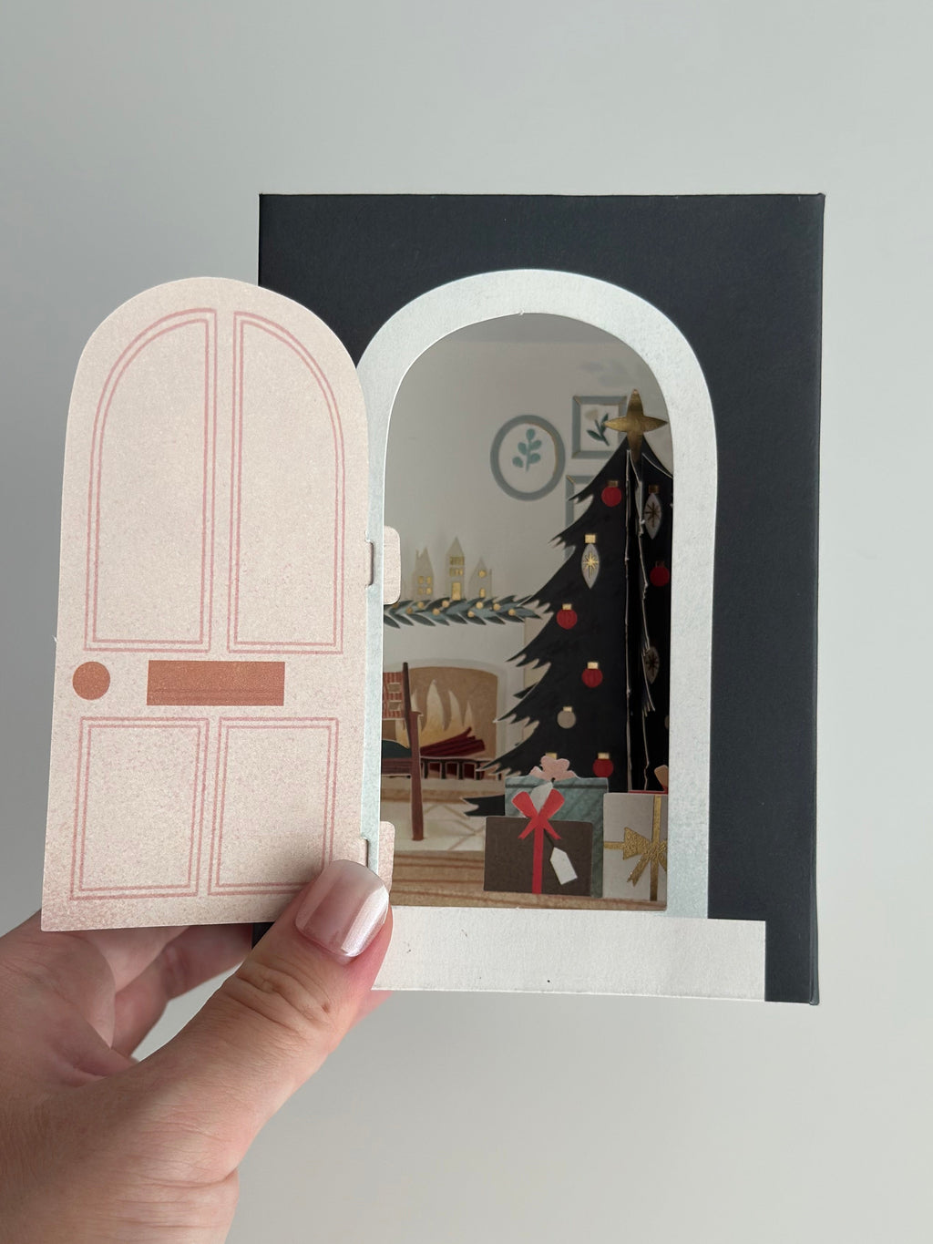 Hand holding closed Christmas door card with wreath and gold details.