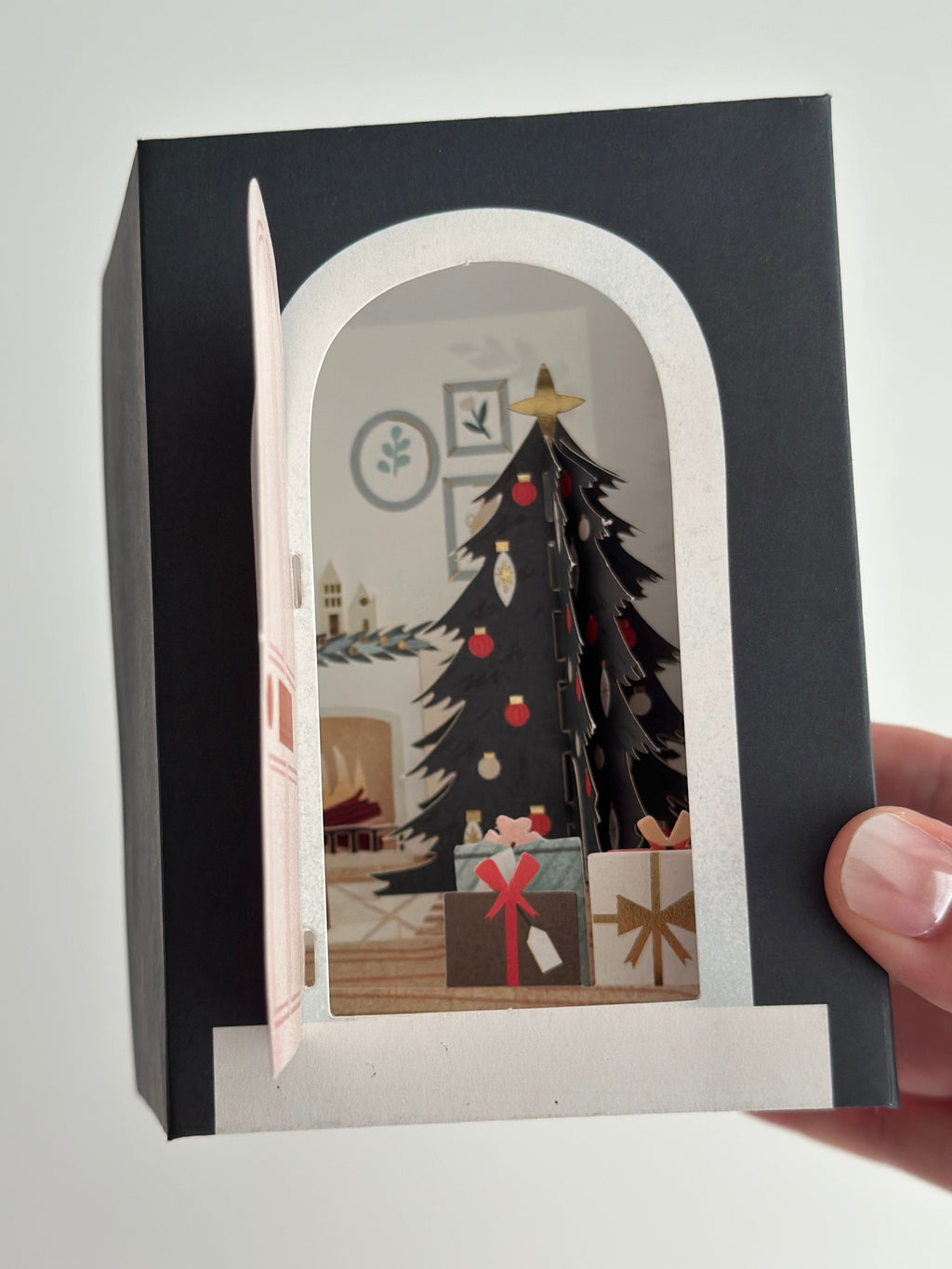 Pop-up Christmas card with door opening to decorated tree and wrapped gifts.