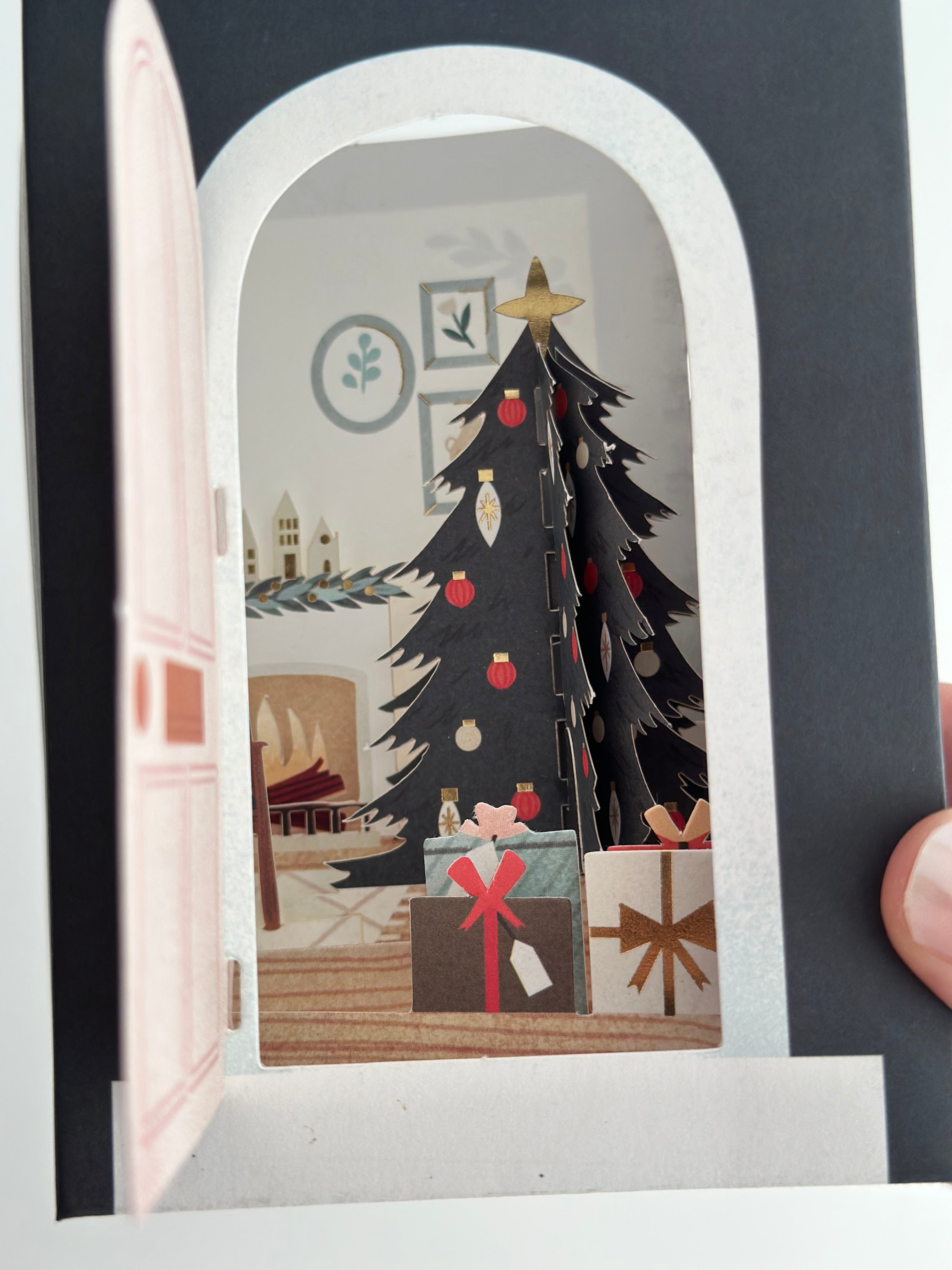 Close-up of pop-up living room with fireplace, black tree, wall art, and gifts.