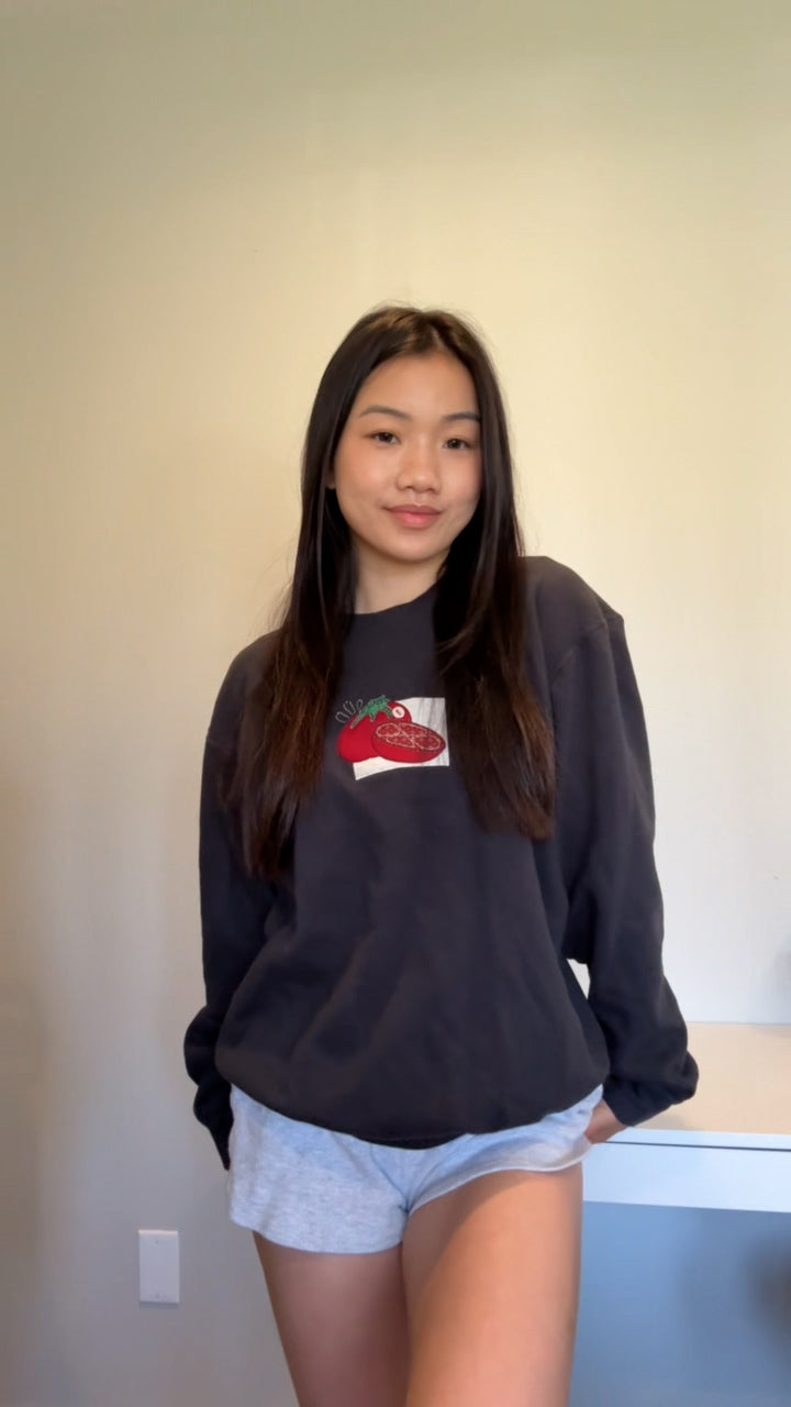 Casual indoor photo of a woman wearing a vintage black tomato embroidered sweatshirt, cozy lightweight crewneck for everyday wear.