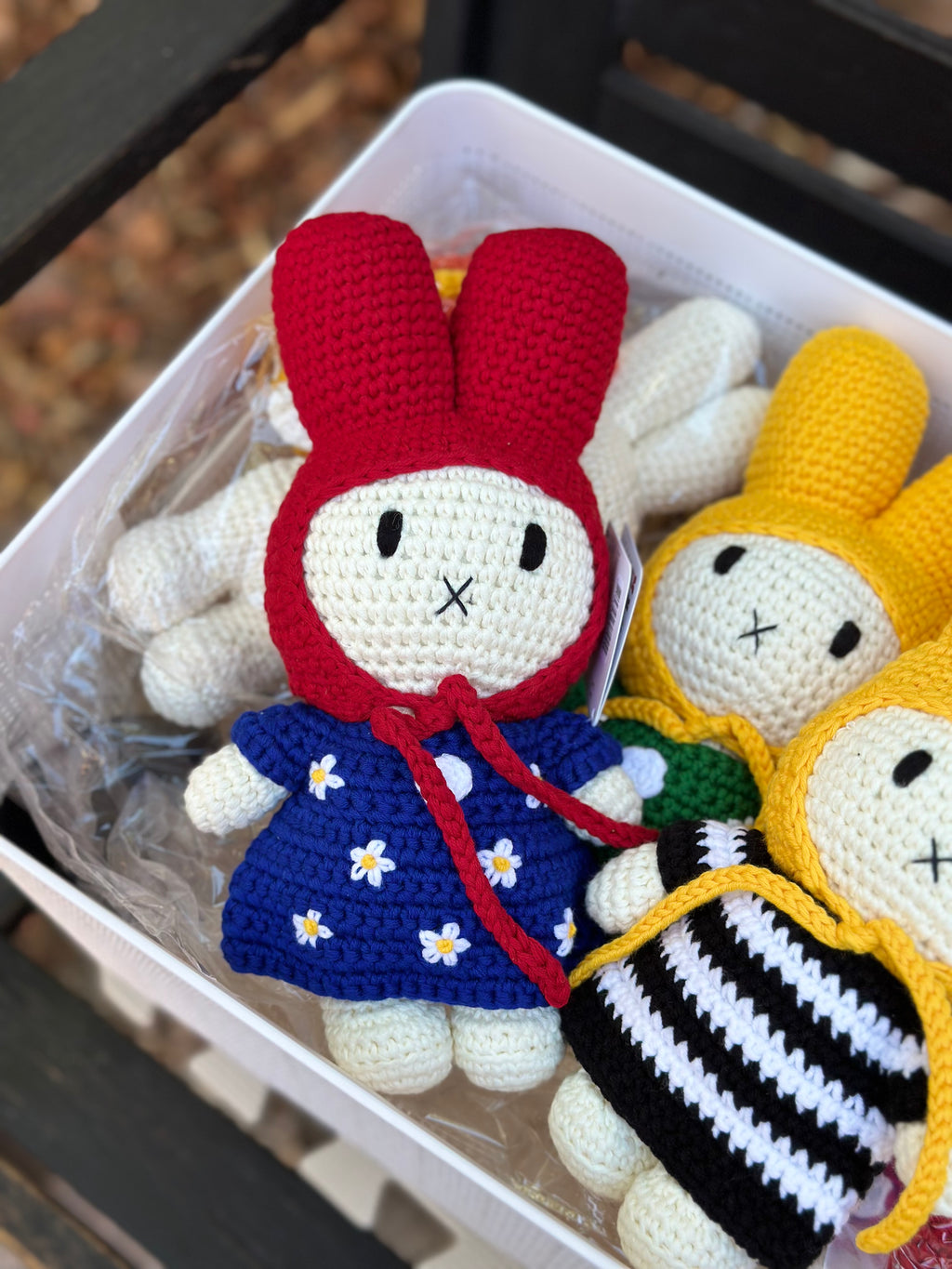 Handmade crochet bunny doll wearing a red hood and blue dress with white daisy flowers, part of the Just Dutch Miffy collection, shown with brown kraft tag.