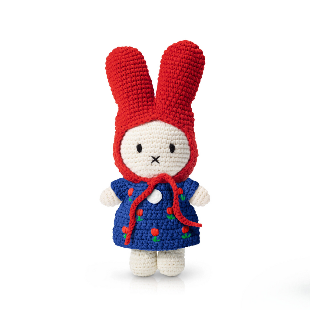 Close-up of handmade crochet bunny doll wearing a red bonnet and deep blue dress with embroidered red tulips — soft and detailed plush toy for collectors or gifting.
