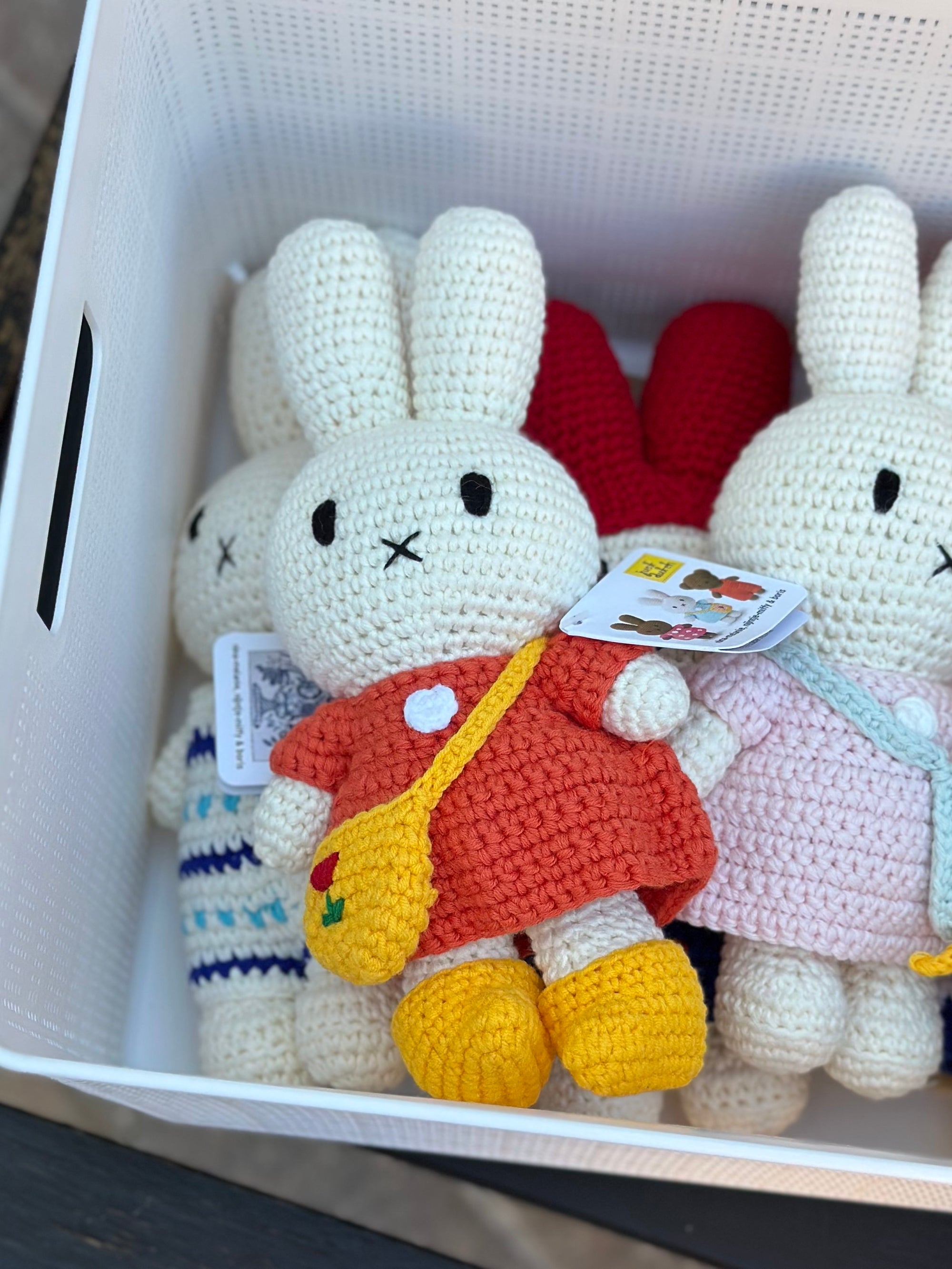 Red dress crochet Miffy plush with tulip bag leaning in a basket alongside pink and striped outfit Miffy dolls.