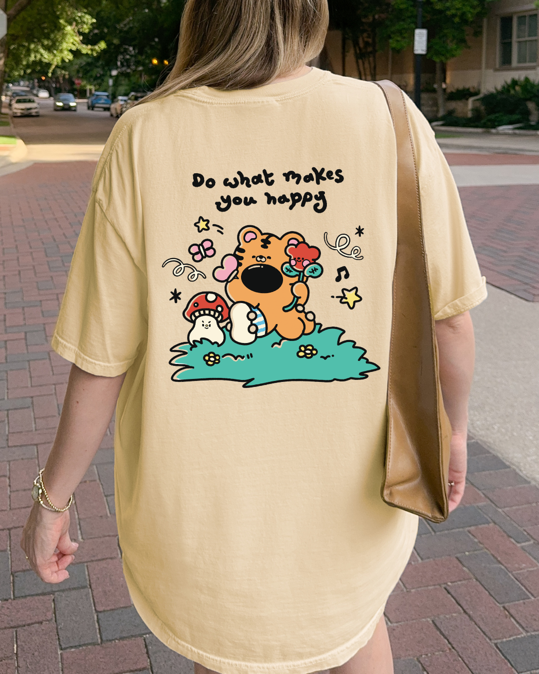 Close up of cute cartoon back graphic on butter yellow t shirt with encouraging do what makes you happy message