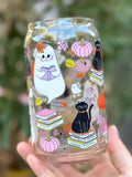 Clear glass can cup showing a black cat on books, a smiling ghost reading, pumpkins, and autumn leaves.