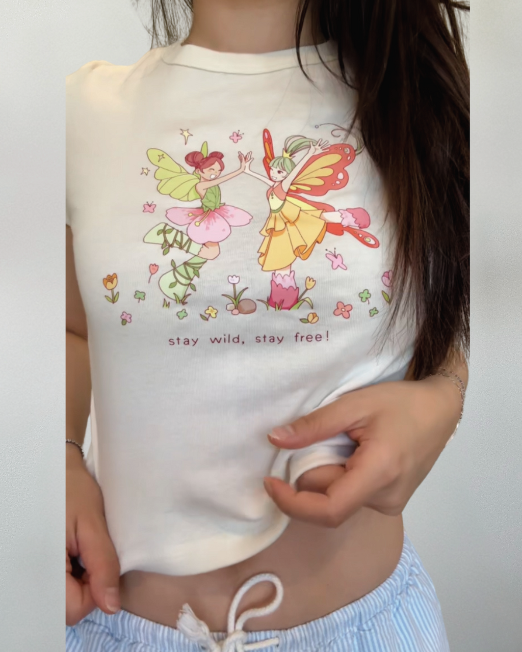 Cropped ivory baby tee with whimsical dancing fairy artwork and floral details