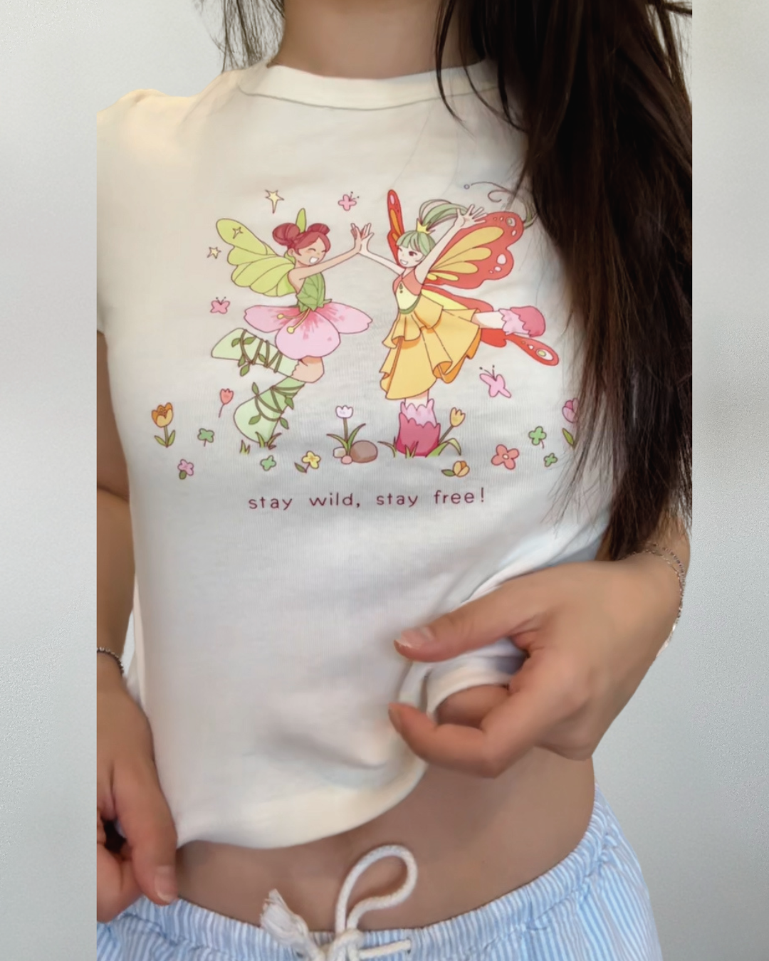 Cropped ivory baby tee with whimsical dancing fairy artwork and floral details
