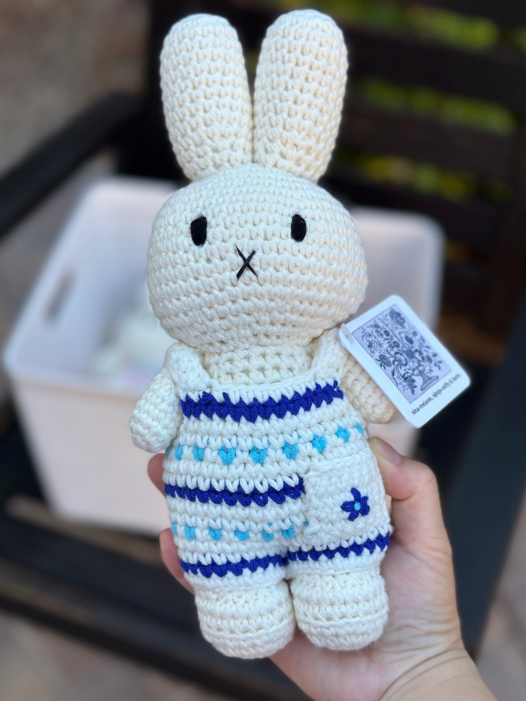 Delft blue crochet Miffy plush in floral jumpsuit held in front of a basket of other handmade dolls.