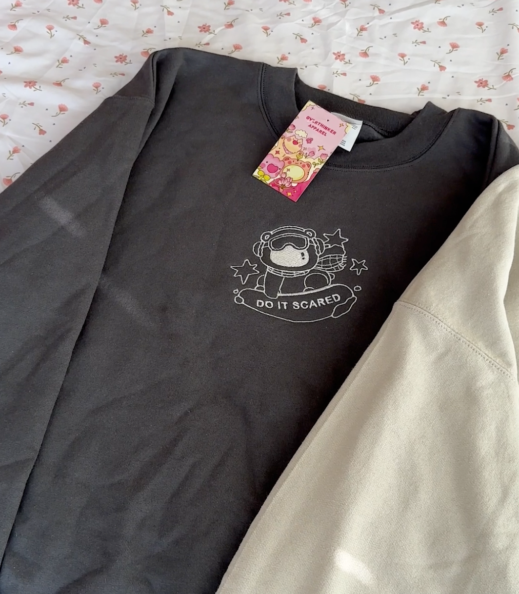 Close-up of embroidered polar bear and “Do It Scared” text stitched on a charcoal gray oversized sweatshirt, showing detailed linework and in-house embroidery.