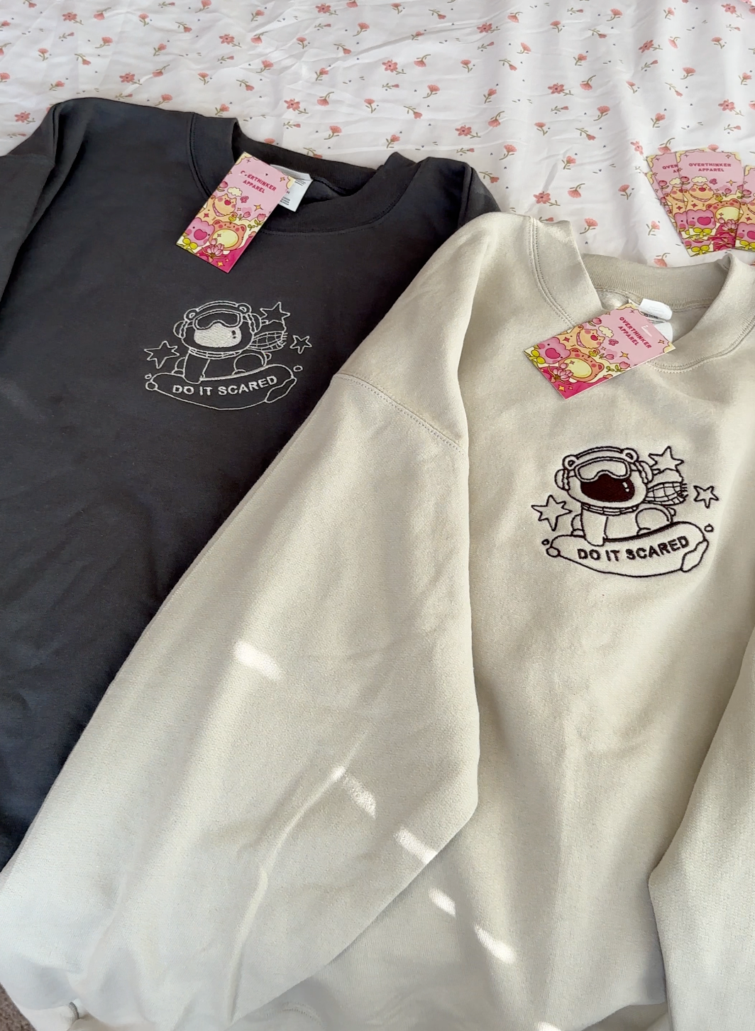 Beige and charcoal gray oversized embroidered sweatshirts featuring a polar bear and “Do It Scared” message, shown side by side to display color options.