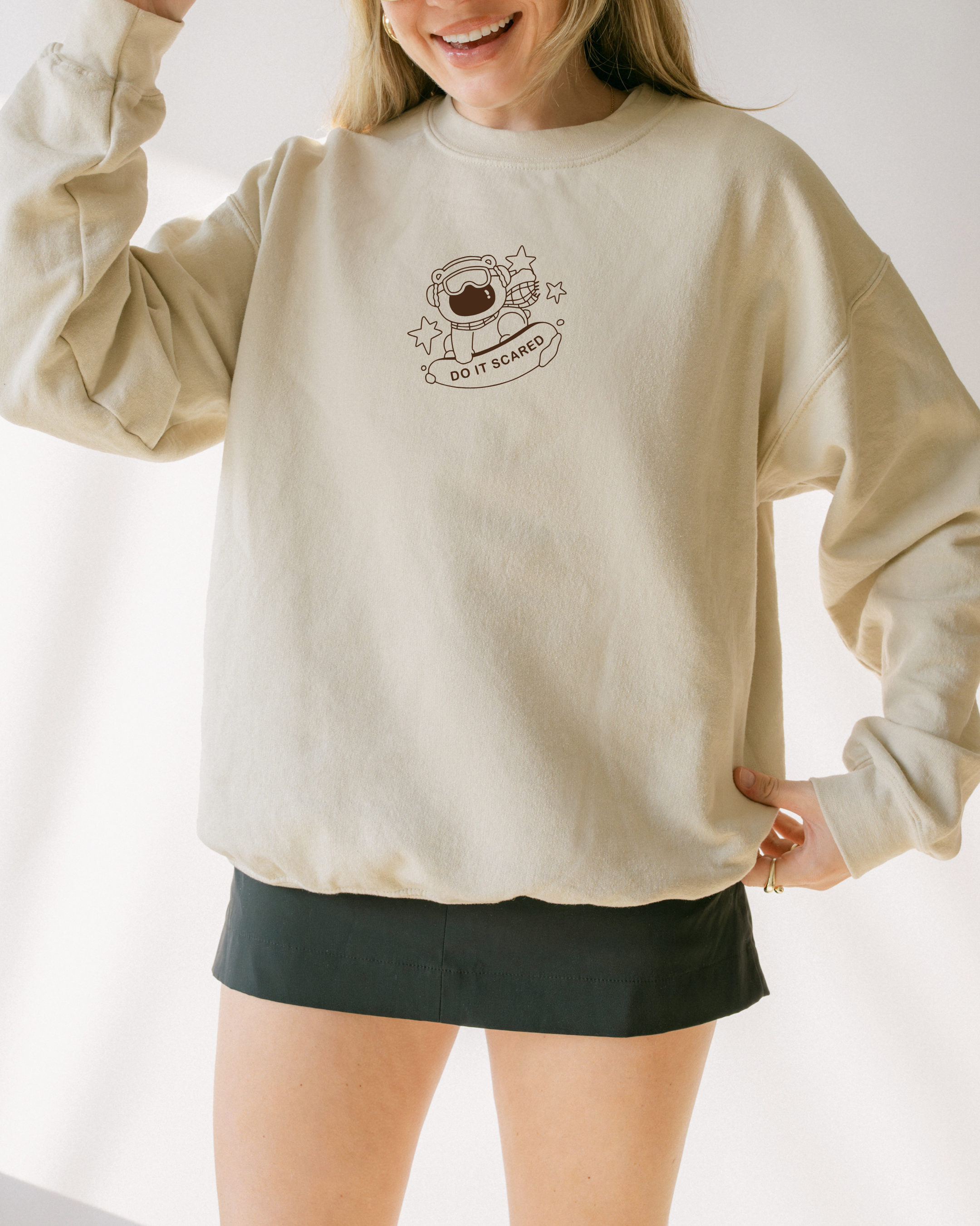 Model wearing an oversized beige embroidered sweatshirt featuring a polar bear illustration and the phrase “Do It Scared,” styled for calm motivational everyday wear.