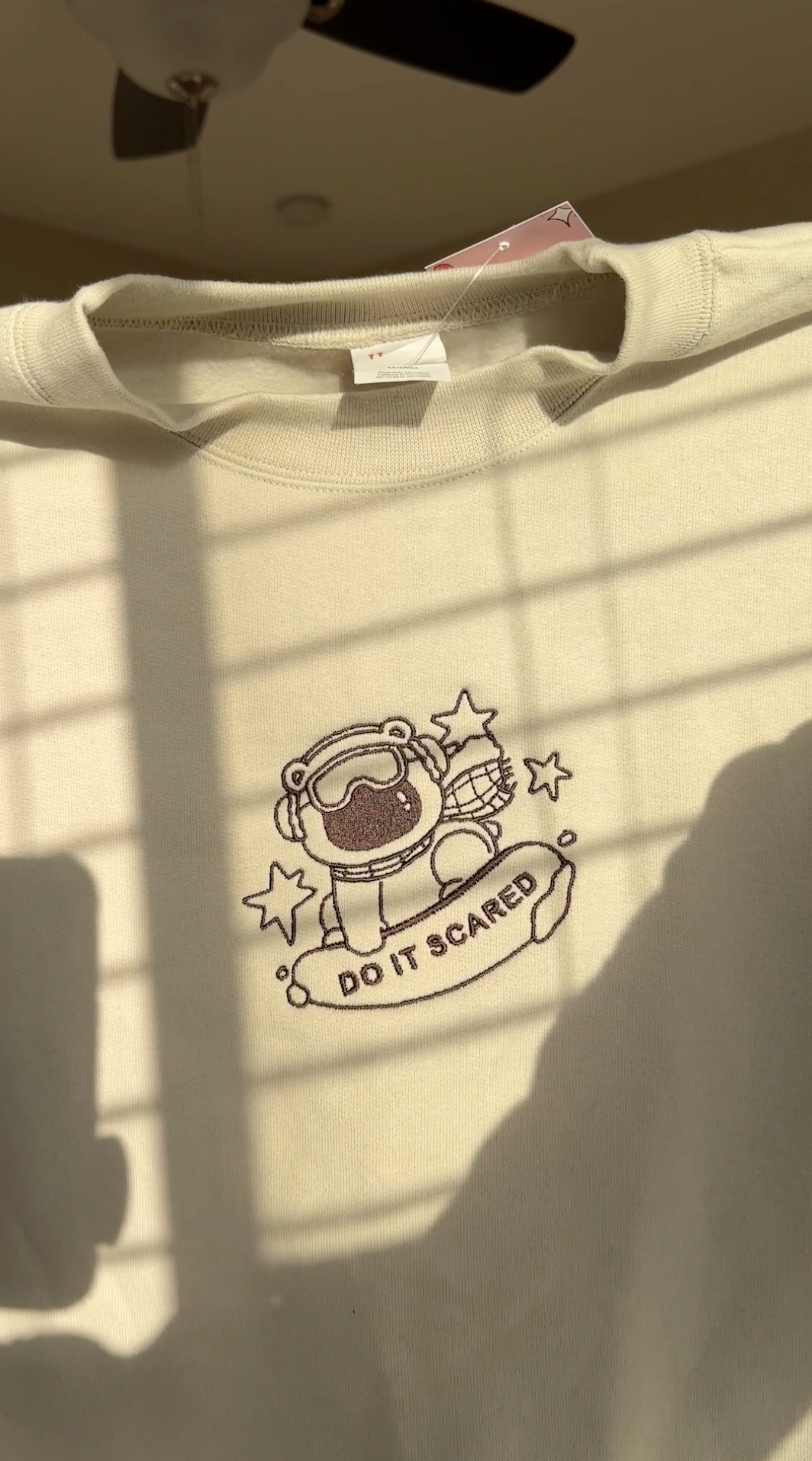 Close-up of polar bear embroidery with “Do It Scared” text stitched on a beige oversized sweatshirt, highlighting fine stitching and minimal linework.