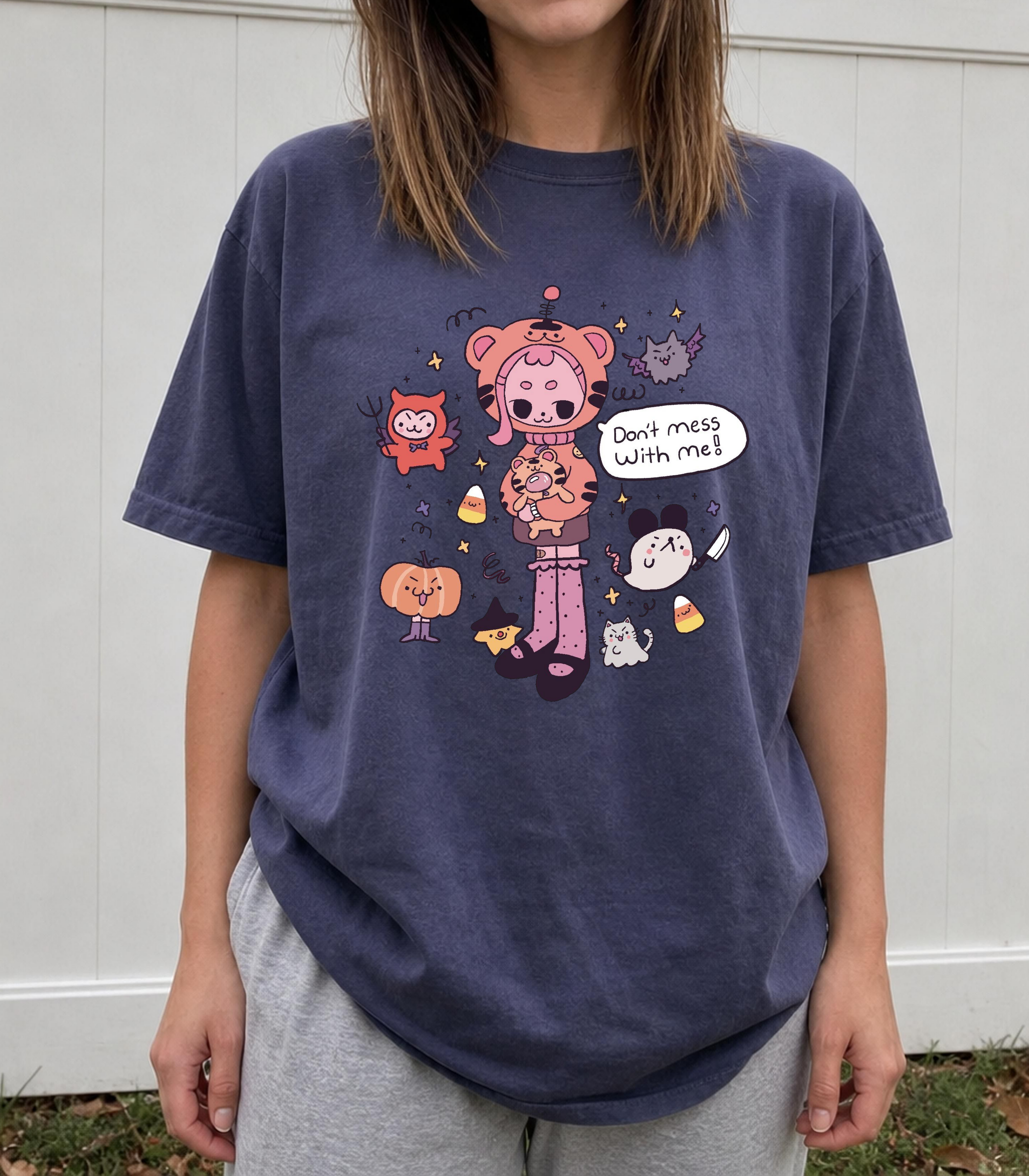 A person wearing an oversized navy graphic T-shirt with a colorful cartoon illustration and the text 'Don't mess with me.' The photo is taken outdoors against a white paneled wall, with the person's torso, arms, and part of the legs visible.