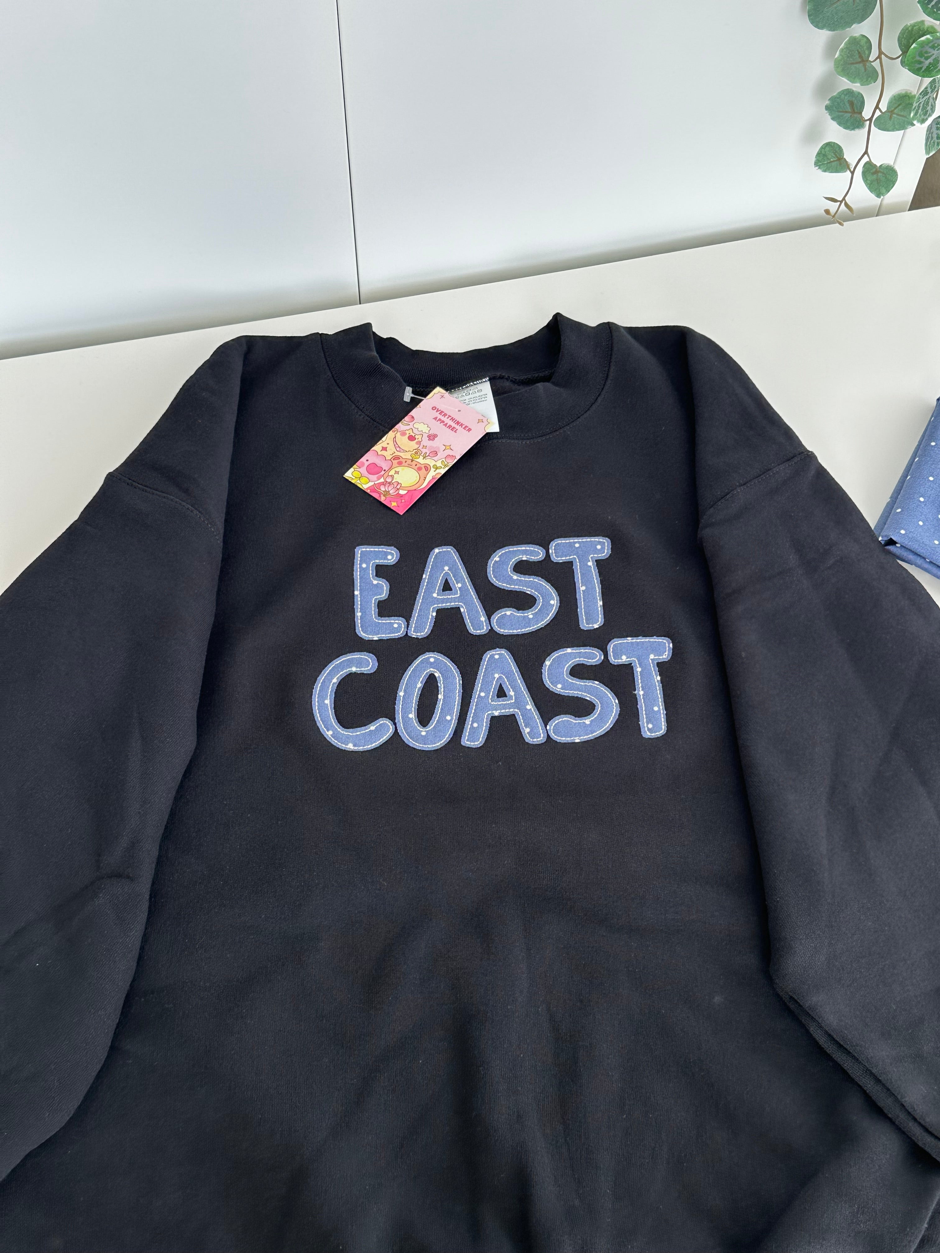 close view of black east coast embroidered sweatshirt folded showing detail cozy handmade feel