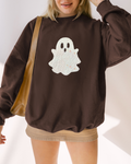 Person standing wearing a brown sweatshirt with embroidered ghost, paired with mini skirt and shoulder bag.