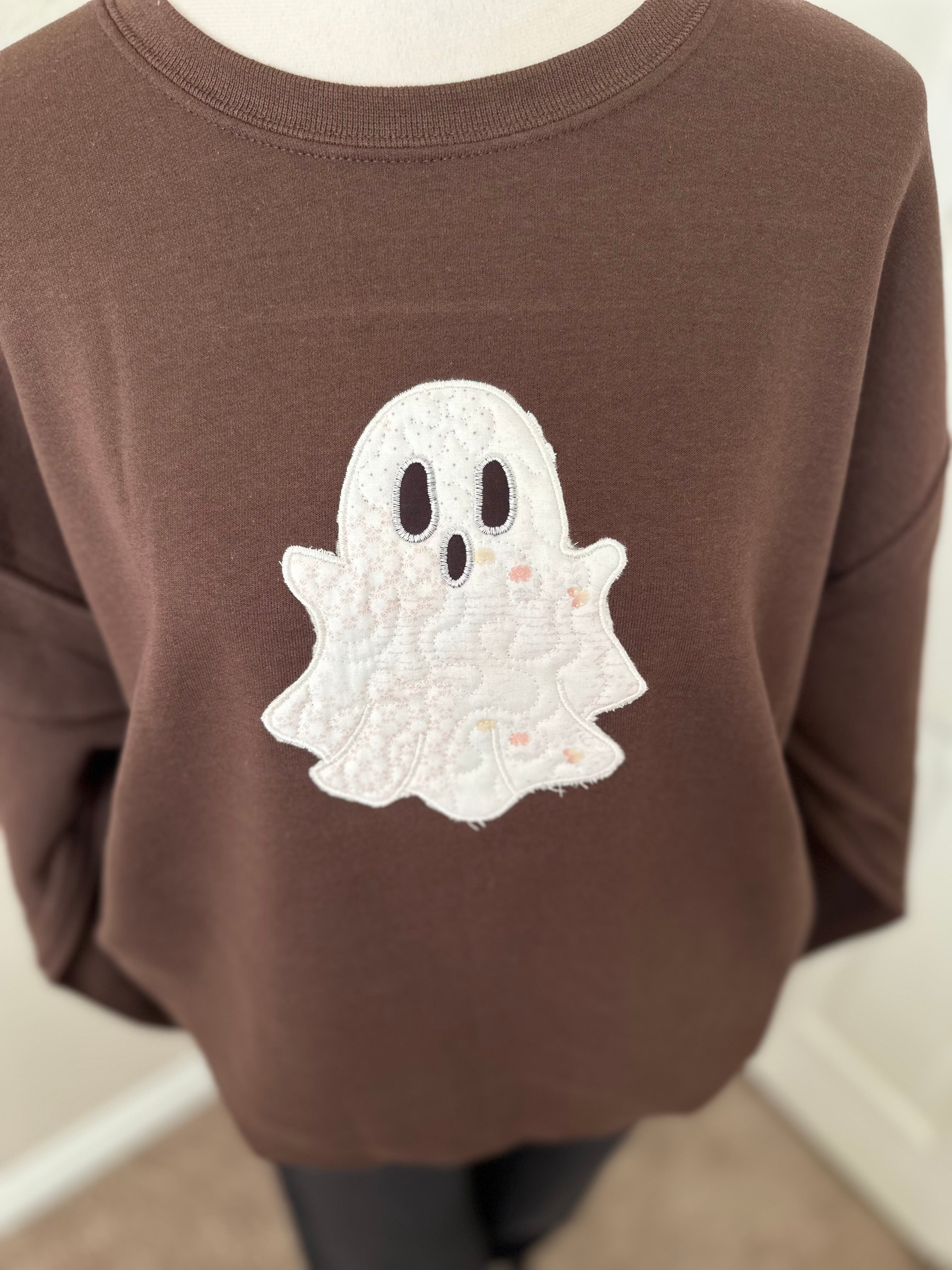 Close-up of white embroidered ghost with stitched details on brown sweatshirt.