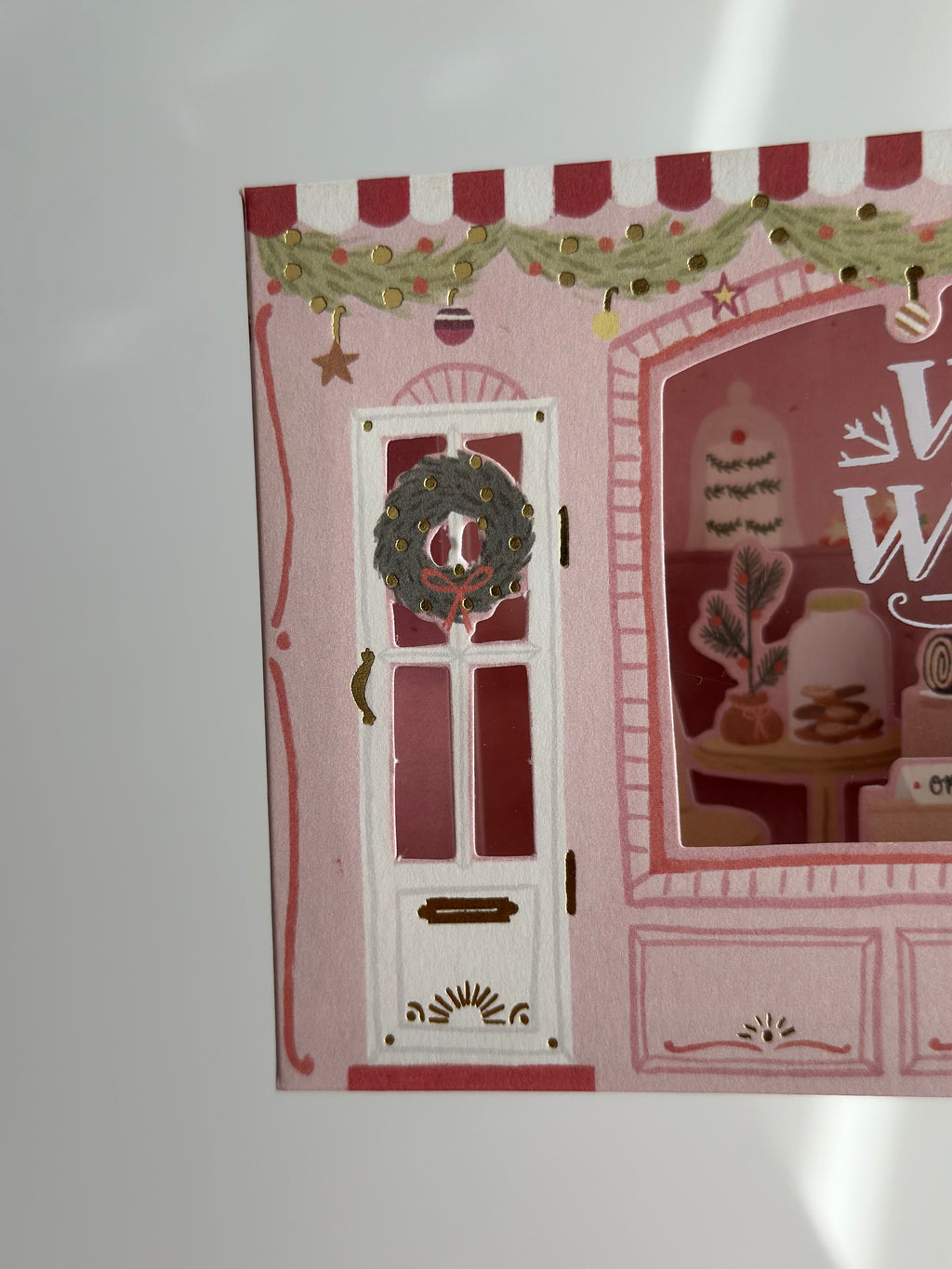Close-up of bakery door with wreath, pink awning, and gold foil garland.