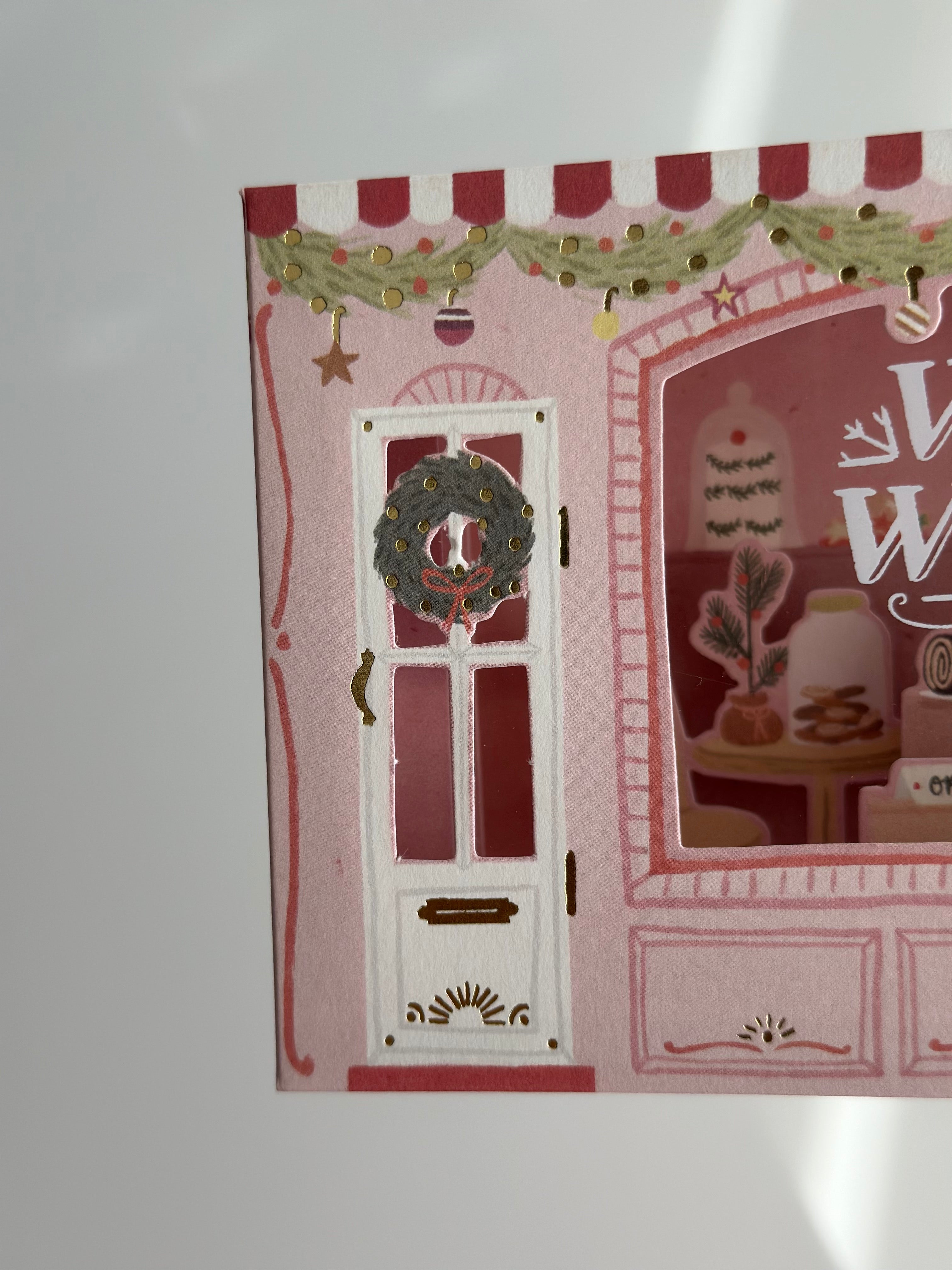 Close-up of bakery door with wreath, pink awning, and gold foil garland.