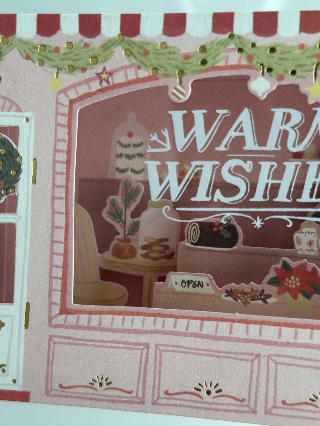 Interior window close-up showing Yule log, cookies, poinsettia, and “open” sign.