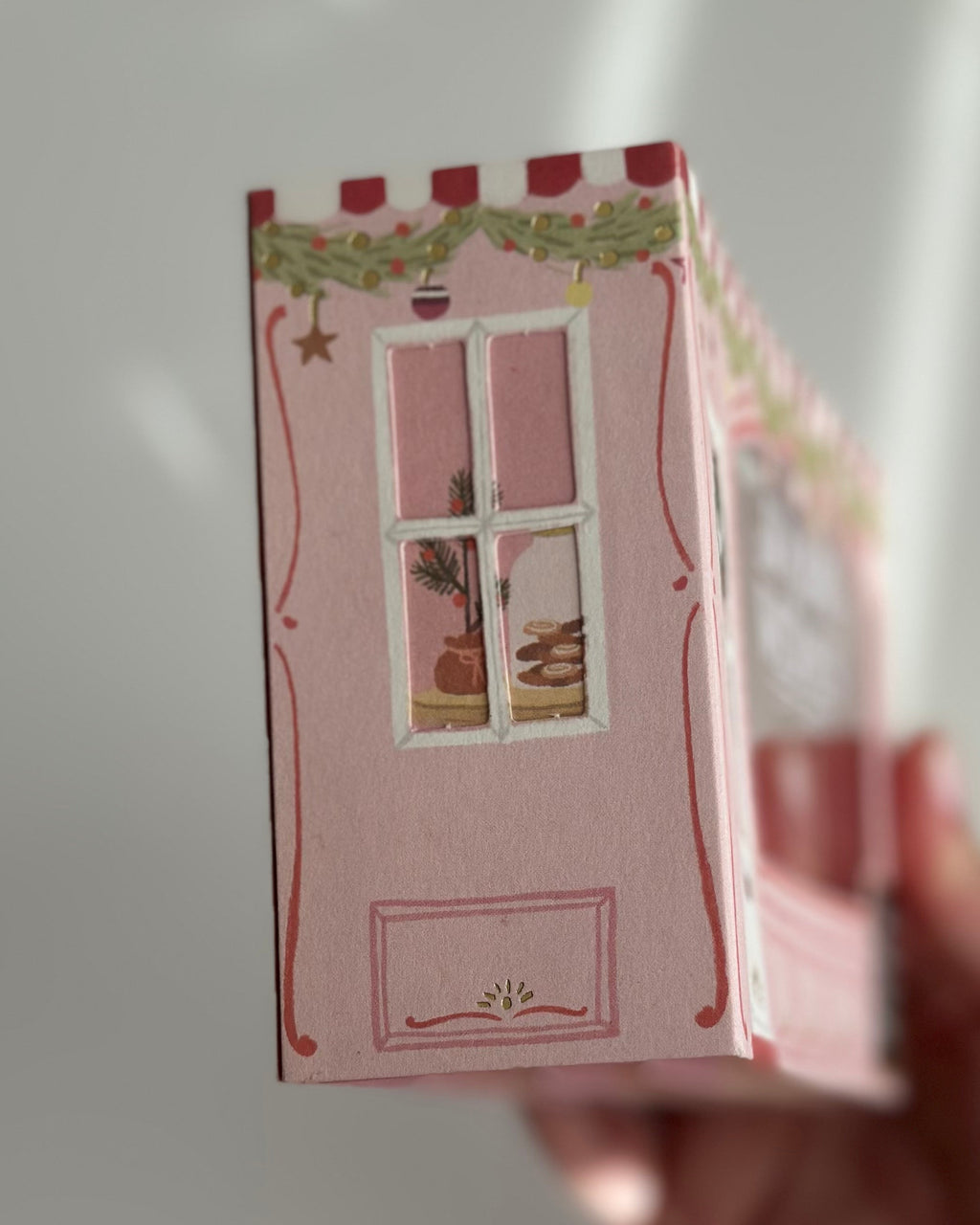 Pink bakery pop-up Christmas card side window showing pastries and garland.