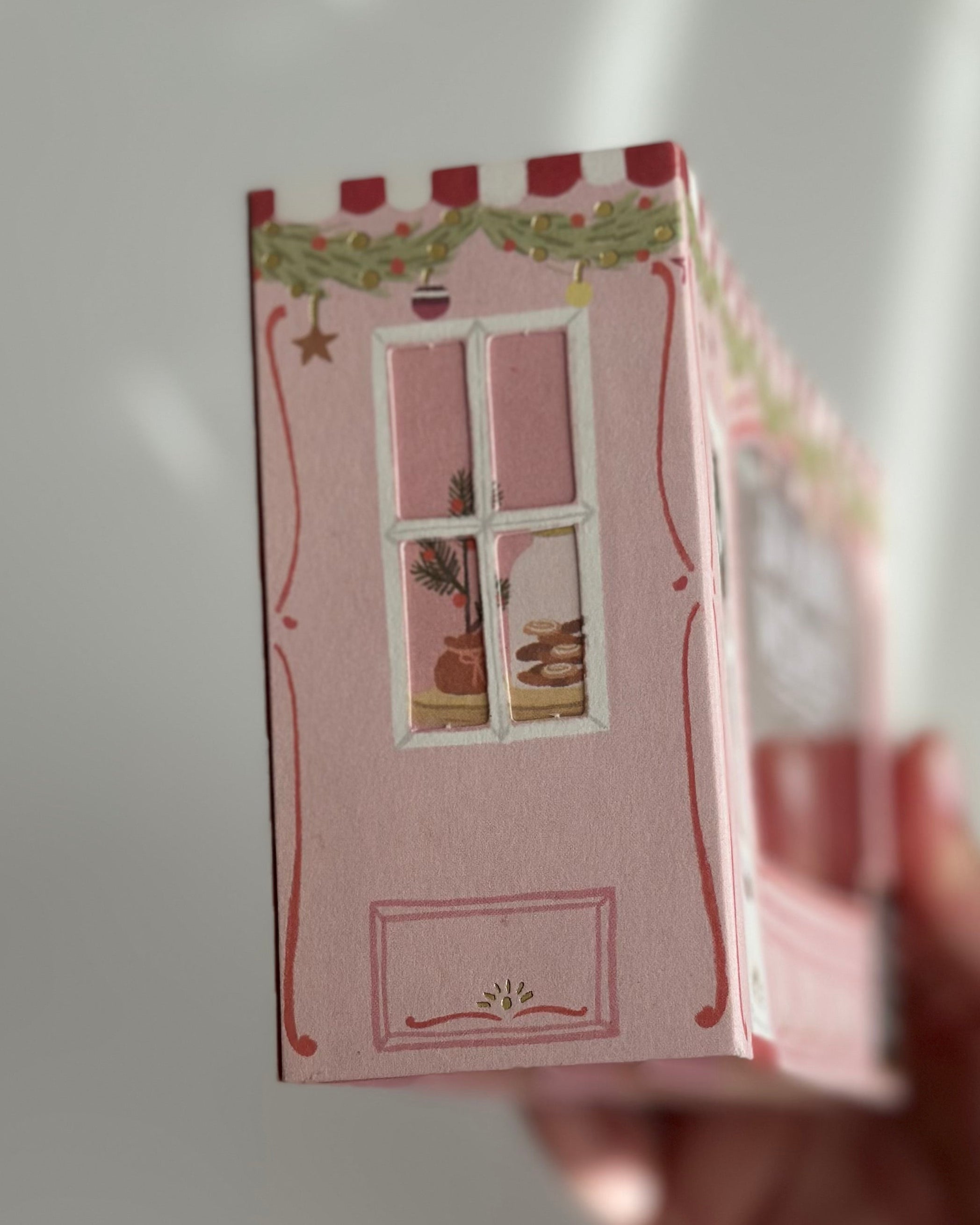 Pink bakery pop-up Christmas card side window showing pastries and garland.