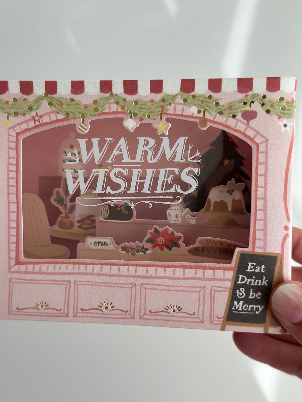 Close-up of “Warm Wishes” lettering with garland and pastries inside the window.