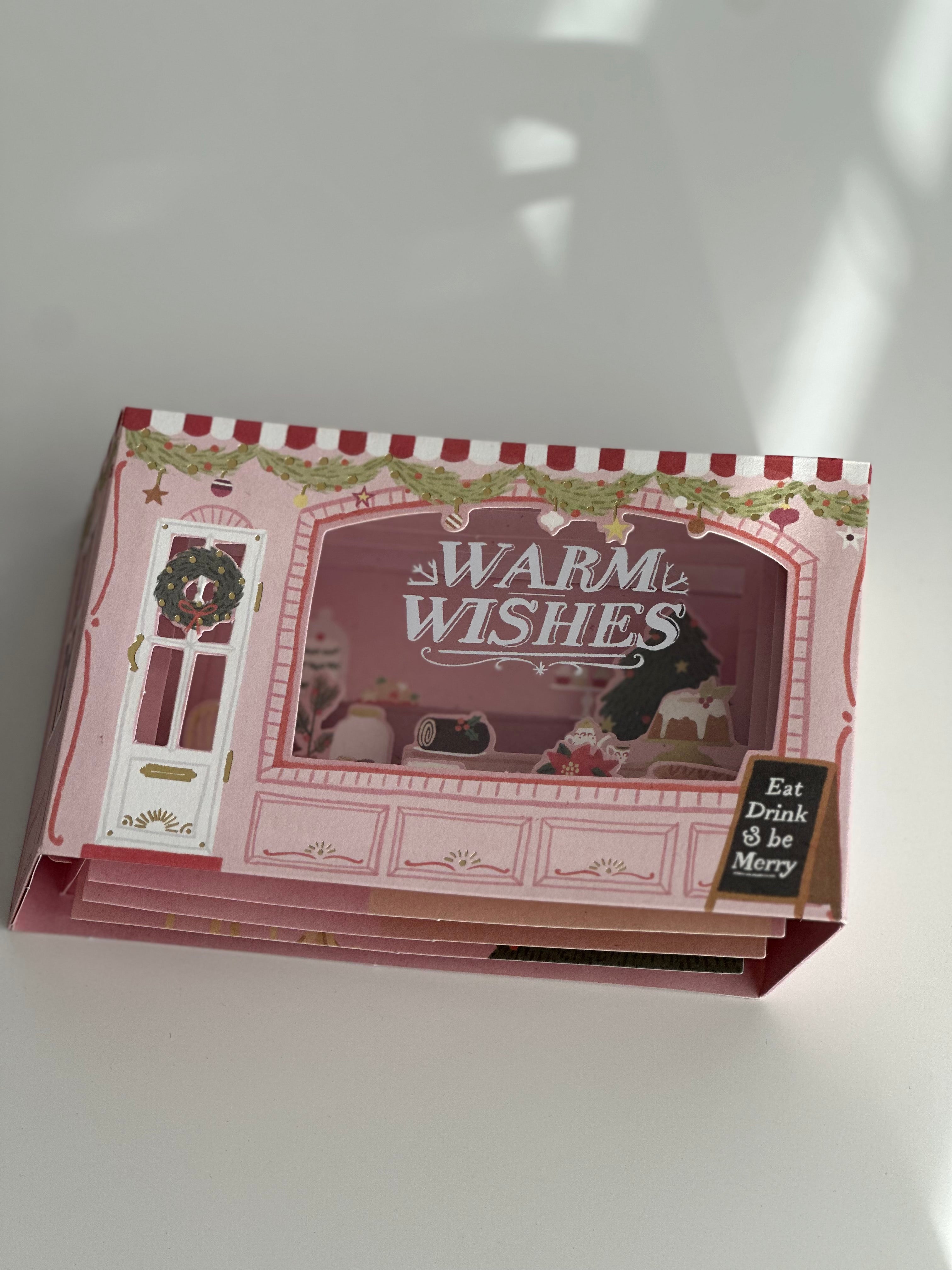 Folded pop-up bakery Christmas card showing layered interior and “Warm Wishes.”