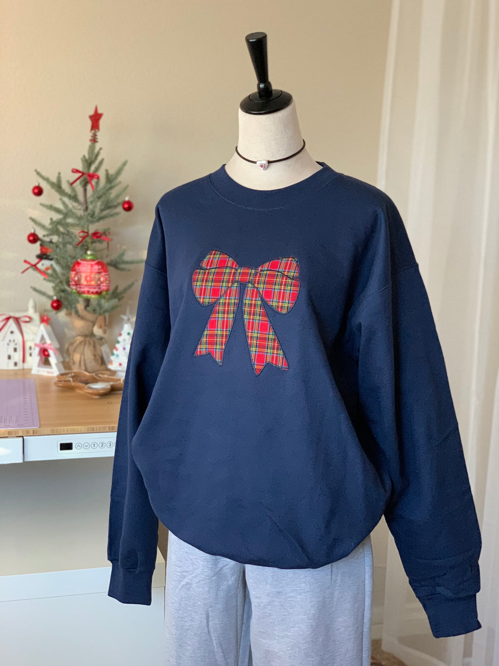 Navy sweatshirt with red plaid bow in cozy room setting with mini tree decor