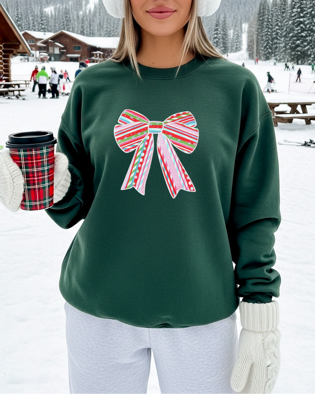 Festive forest green holiday sweatshirt with embroidered candy cane bow, styled for winter with earmuffs and gloves at a snowy Christmas setting