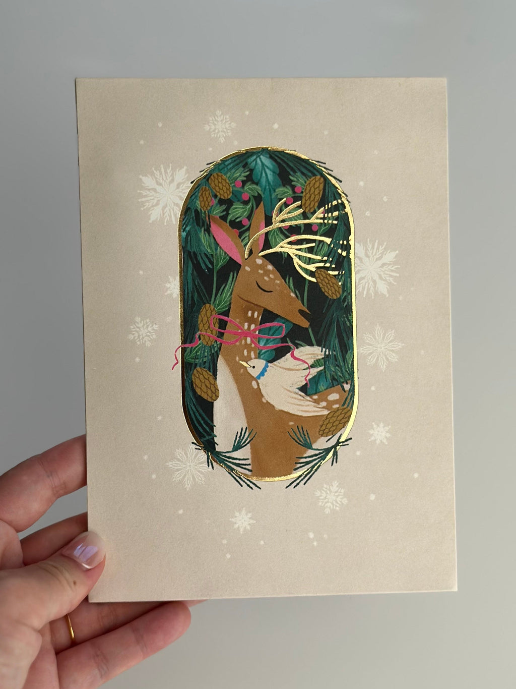Hand holding festive deer Christmas card with gold foil details.