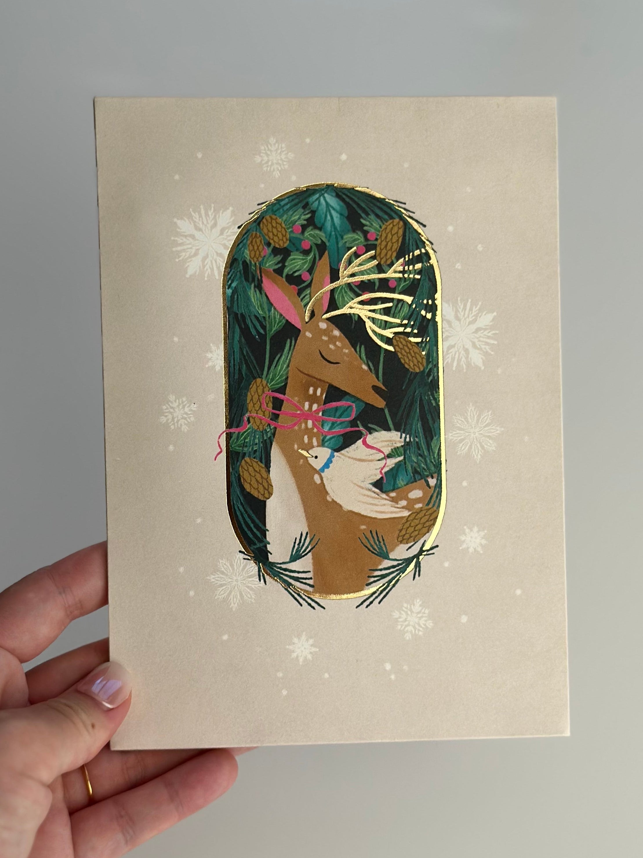 Hand holding festive deer Christmas card with gold foil details.