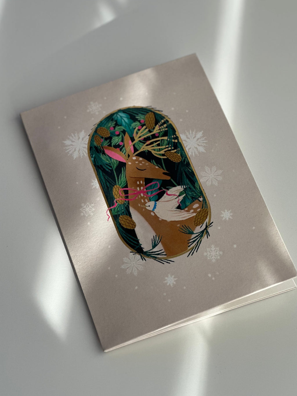 Gold foil deer holiday card angled view with winter greenery and snowflakes.