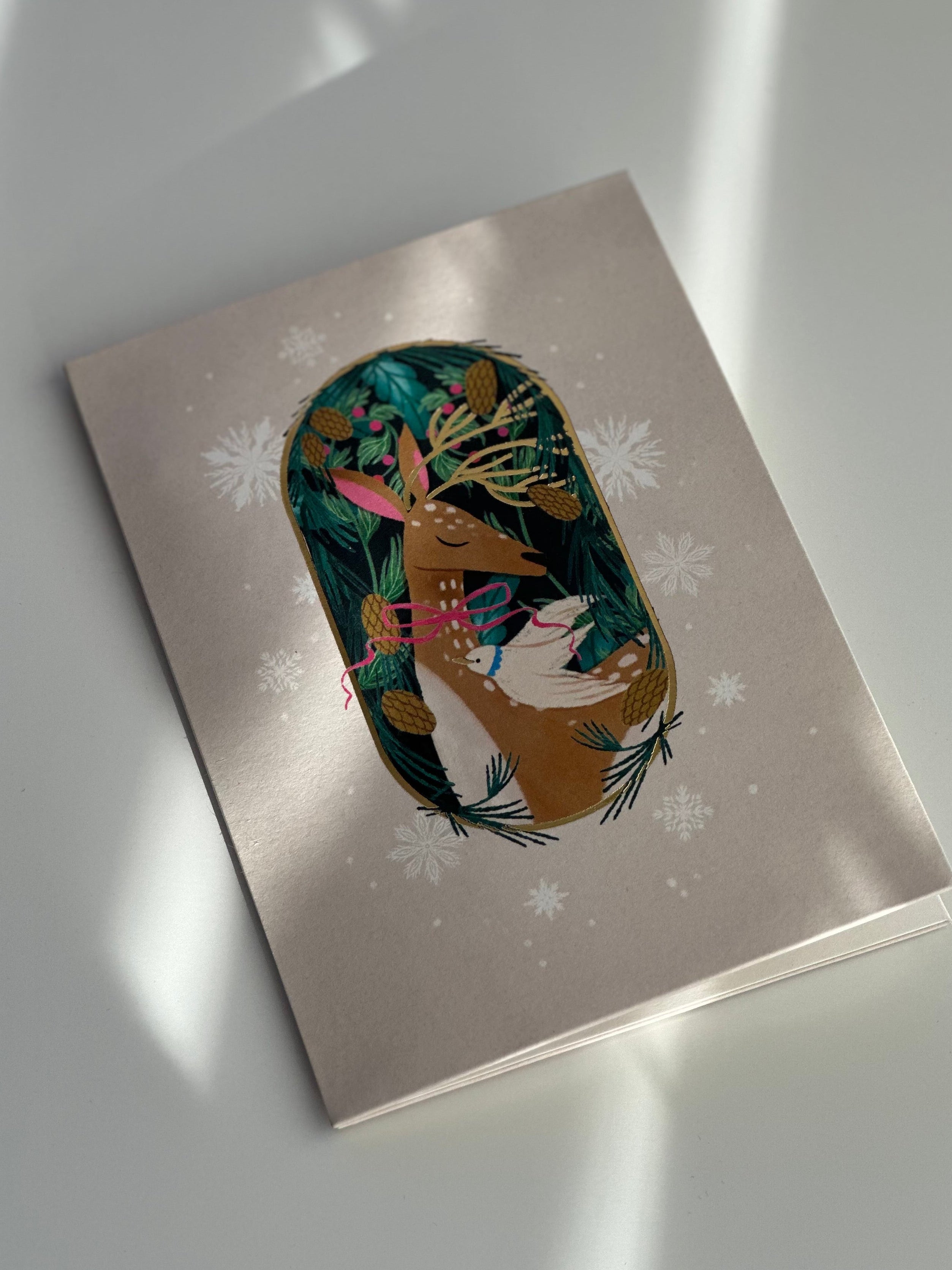 Gold foil deer holiday card angled view with winter greenery and snowflakes.