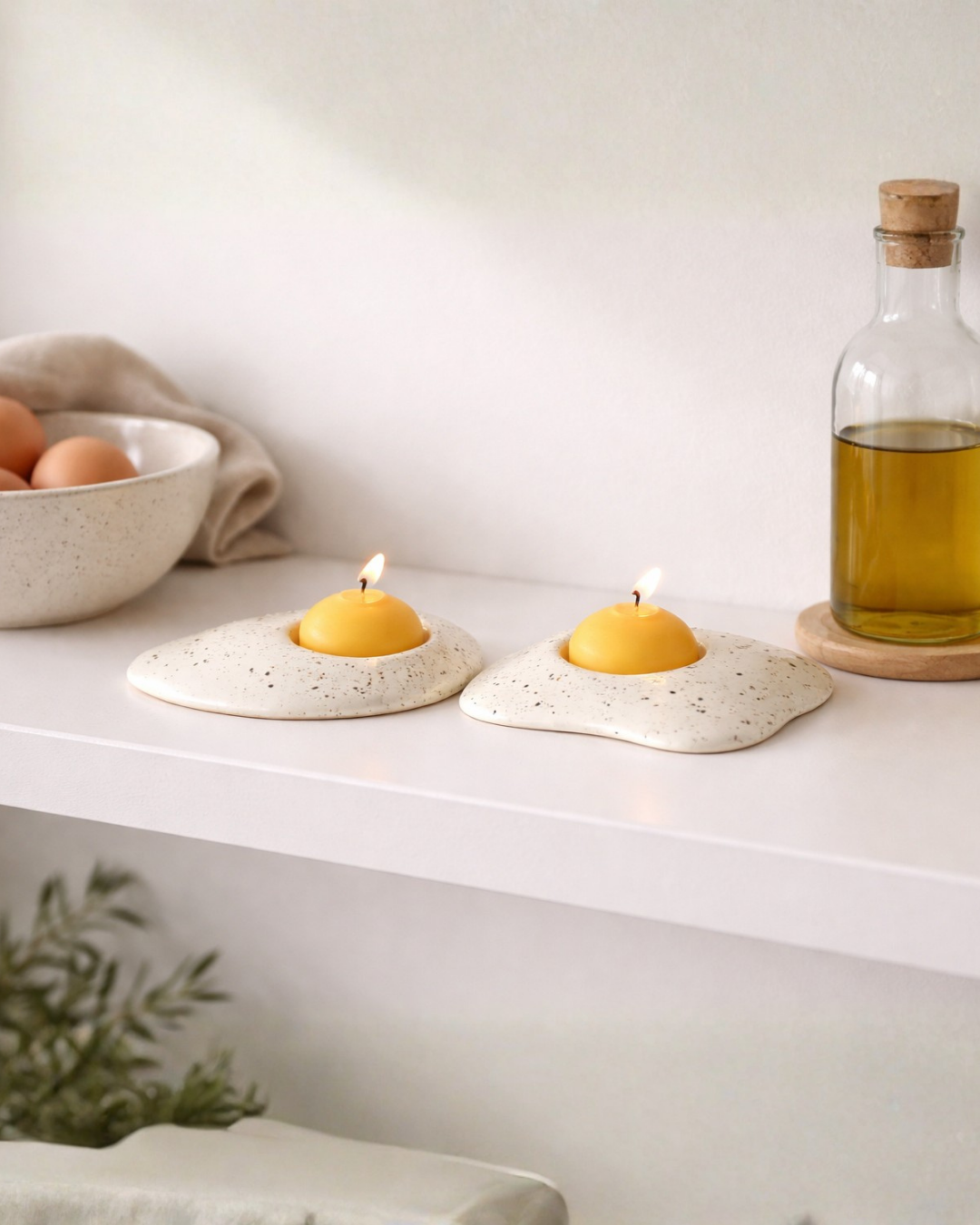 Pair of fried egg candles displayed on kitchen shelf with olive oil bottle and eggs, food shaped candle decor for whimsical kitchen styling.