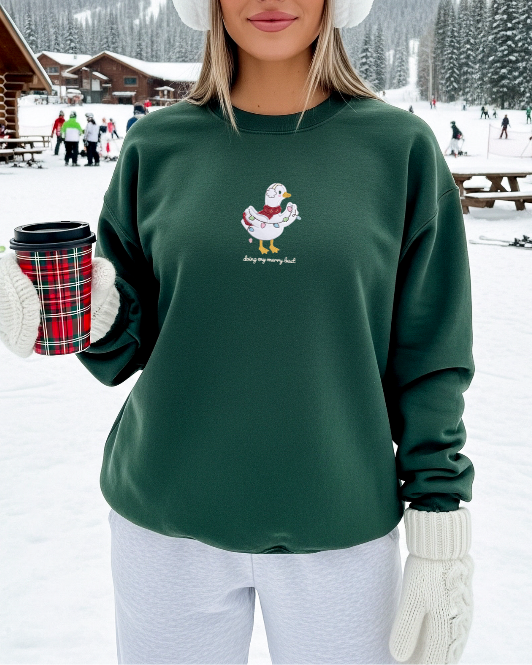 Model wearing a forest green oversized Christmas sweatshirt with an embroidered silly goose tangled in holiday lights, styled outdoors in a snowy winter setting