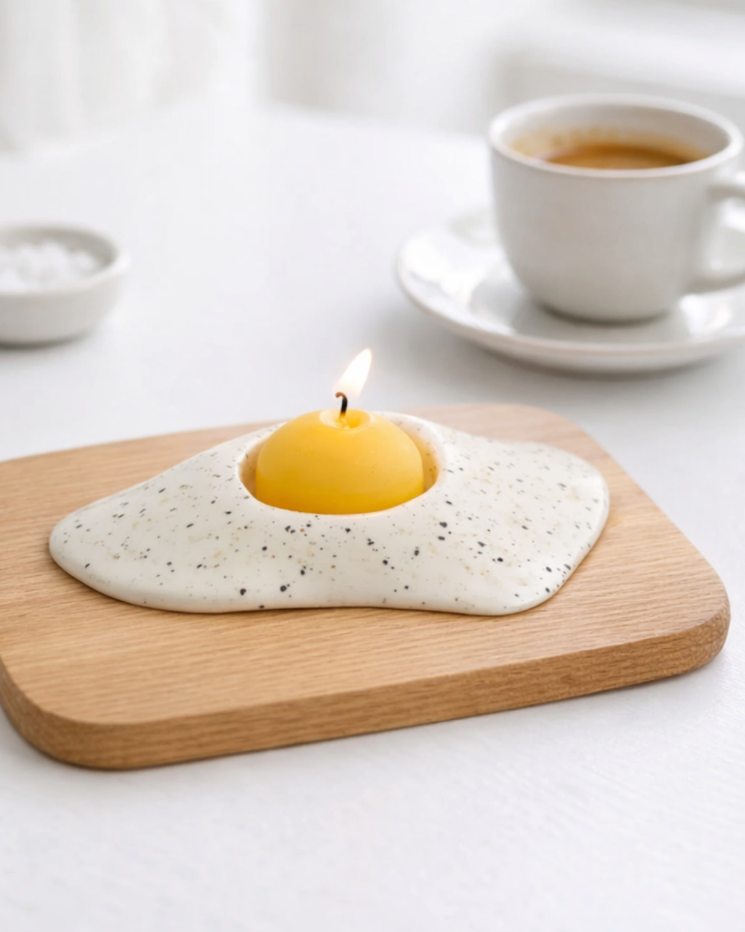 Fried egg candle on wooden board beside espresso cup, novelty food shaped candle for breakfast themed kitchen decor.