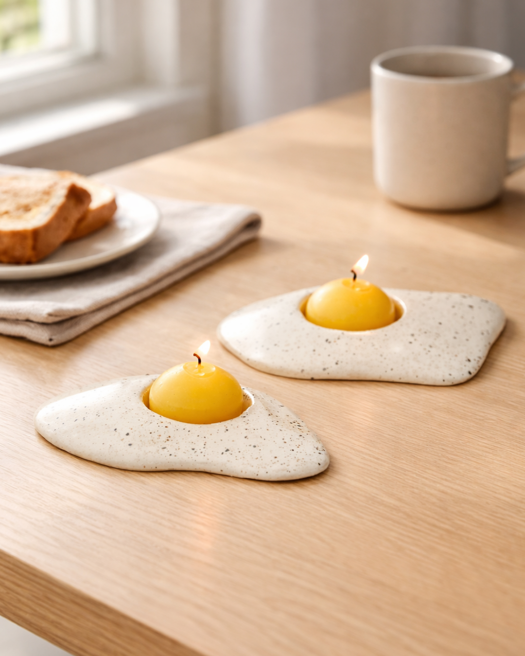 Fried egg candle pair styled on a wooden breakfast table with toast and coffee mug, whimsical food shaped candle for cozy kitchen decor.