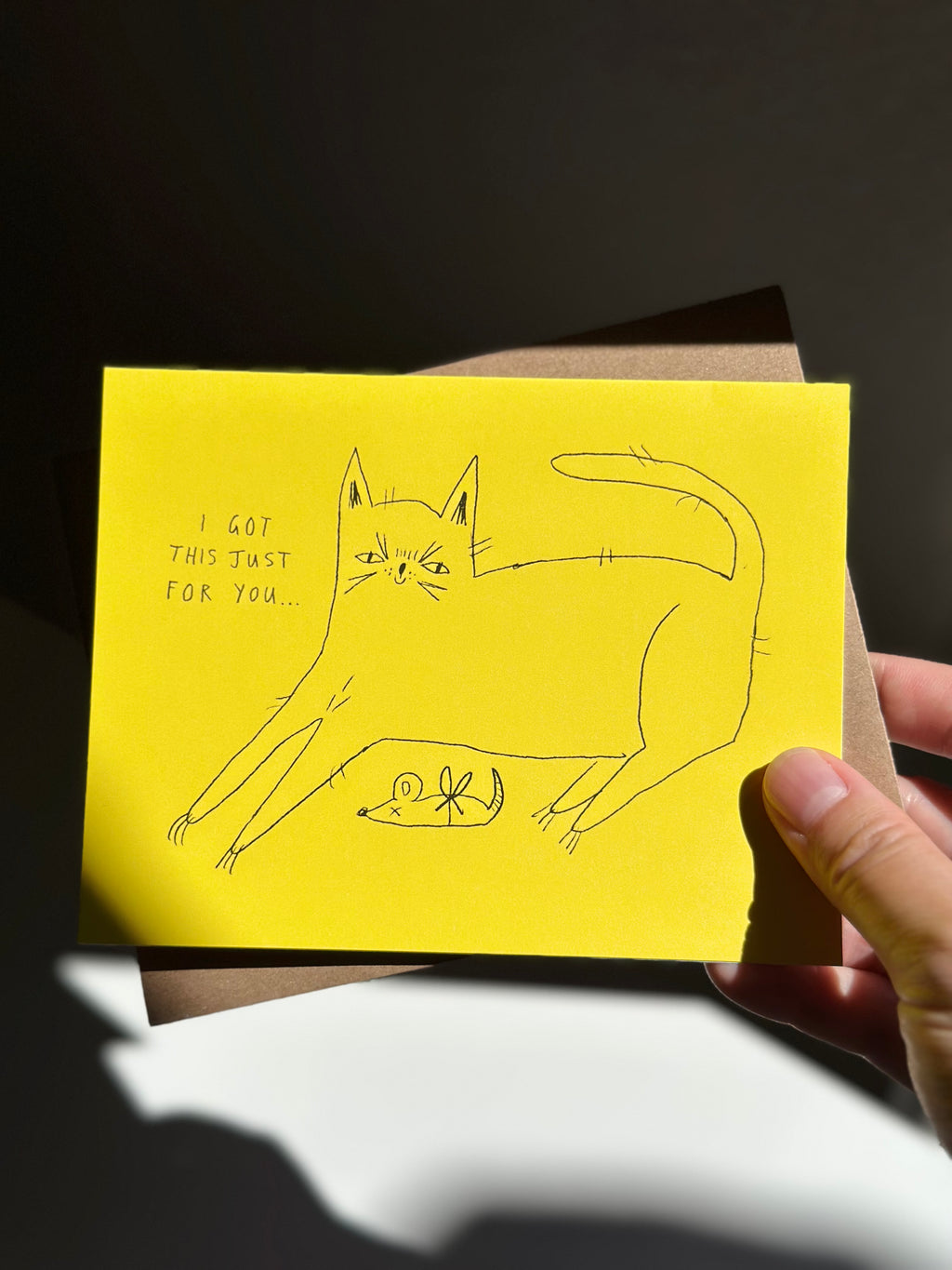 Funny yellow cat greeting card with hand-drawn cat presenting a dead mouse as a gift, captioned ‘I got this just for you…’ with brown kraft envelope.