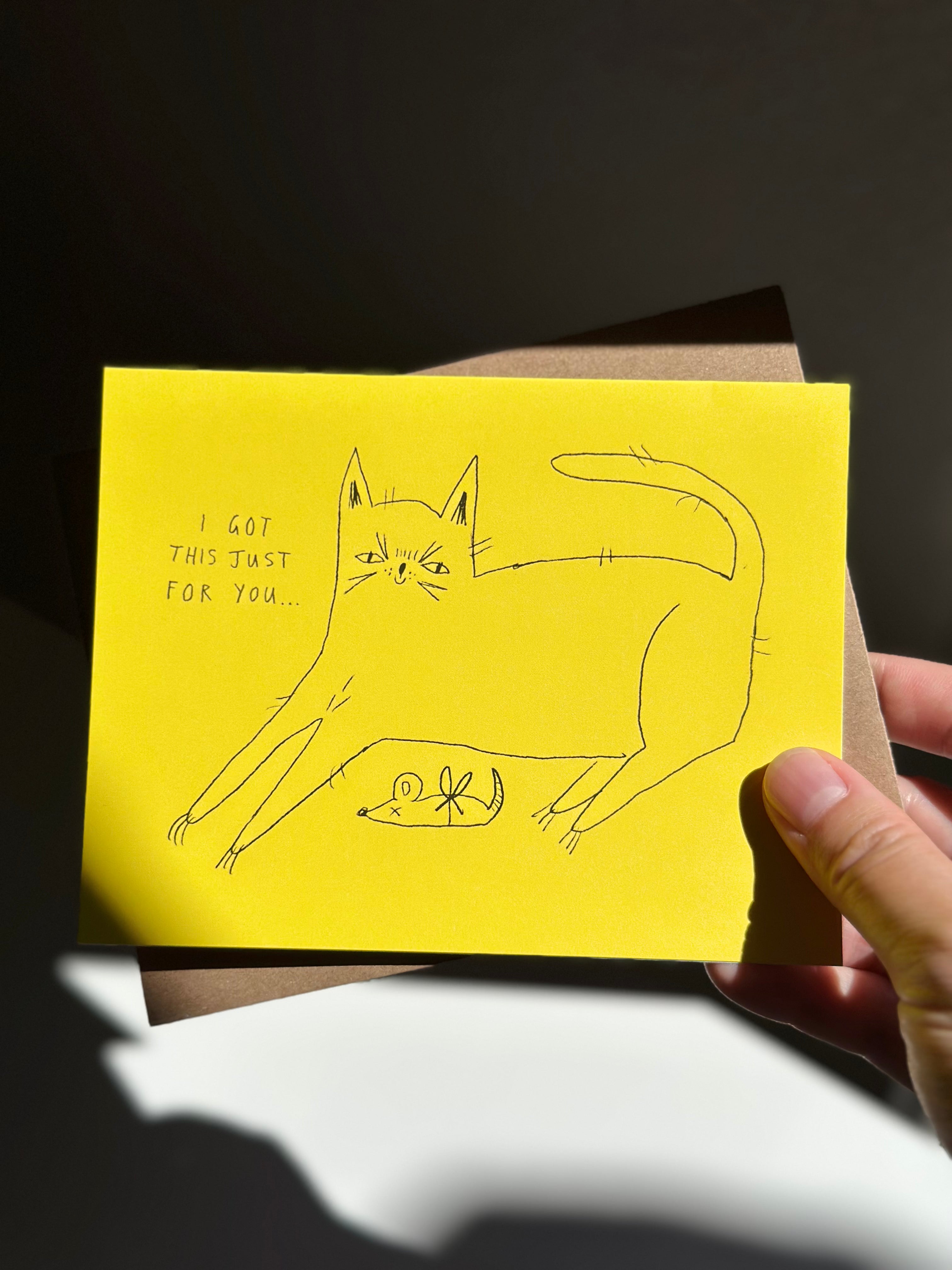 Funny yellow cat greeting card with hand-drawn cat presenting a dead mouse as a gift, captioned ‘I got this just for you…’ with brown kraft envelope.