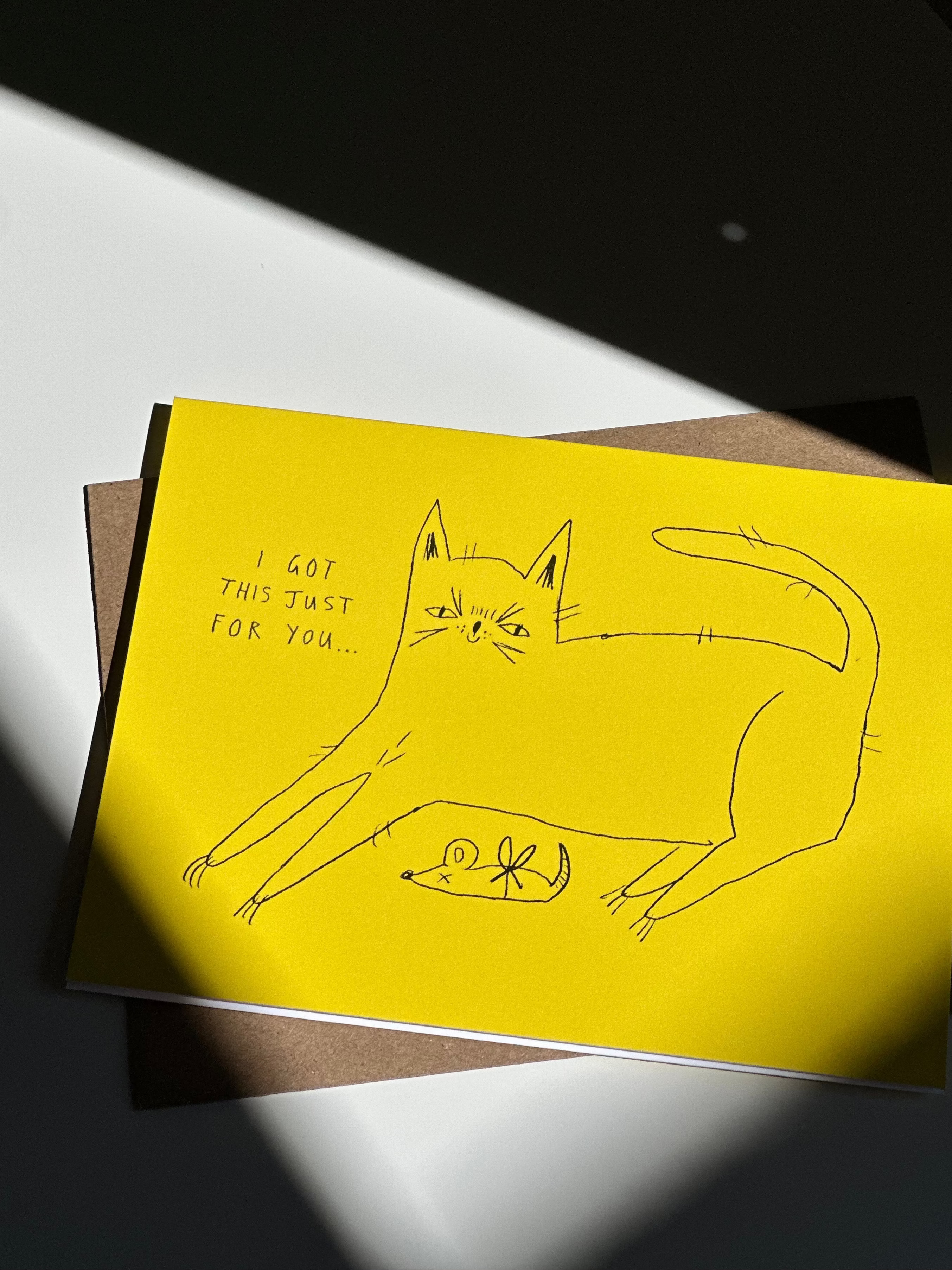 Funny yellow cat greeting card with hand-drawn cat presenting a dead mouse as a gift, captioned ‘I got this just for you…’ with brown kraft envelope.