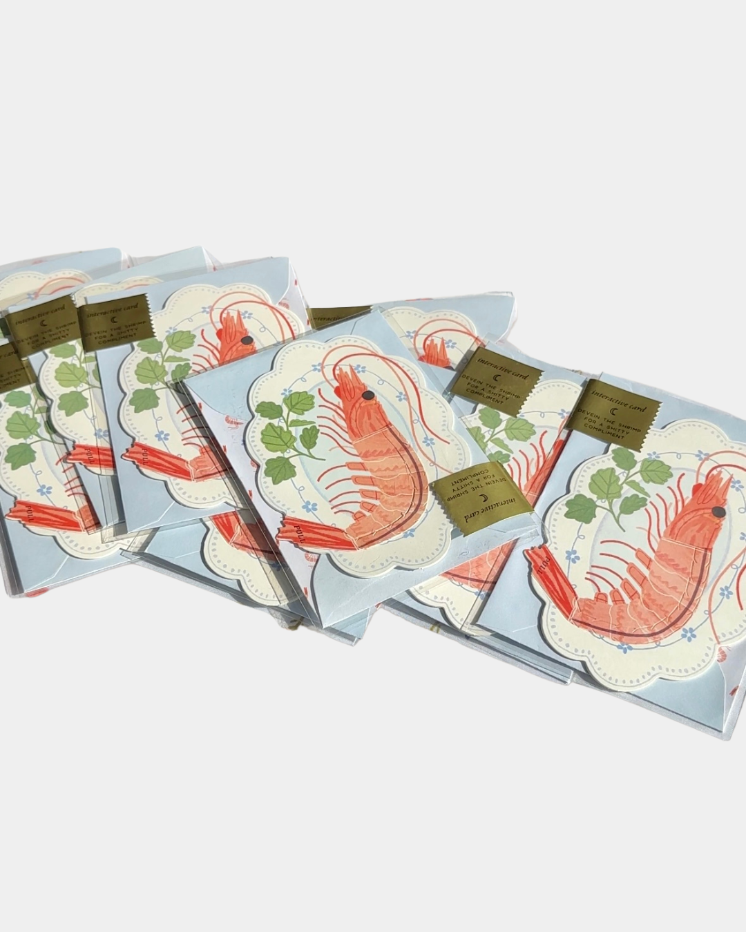 Stack of funny shrimp greeting cards with pun design – “You’re the Sht” interactive peel-to-reveal card.