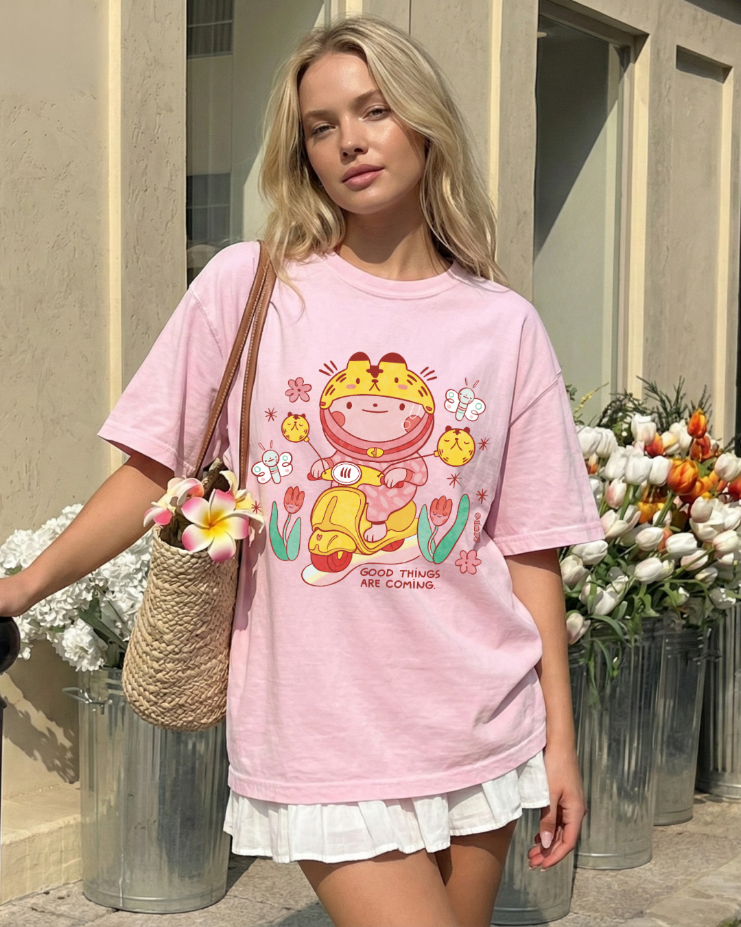 Woman wearing a soft pink graphic tee with a cheerful scooter illustration and the phrase “good things are coming” outdoors