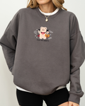 Person wearing a gray sweatshirt with embroidered vampire bear holding pumpkin candy bucket and “Feed Me Sweets” text, layered over a white shirt with shorts.