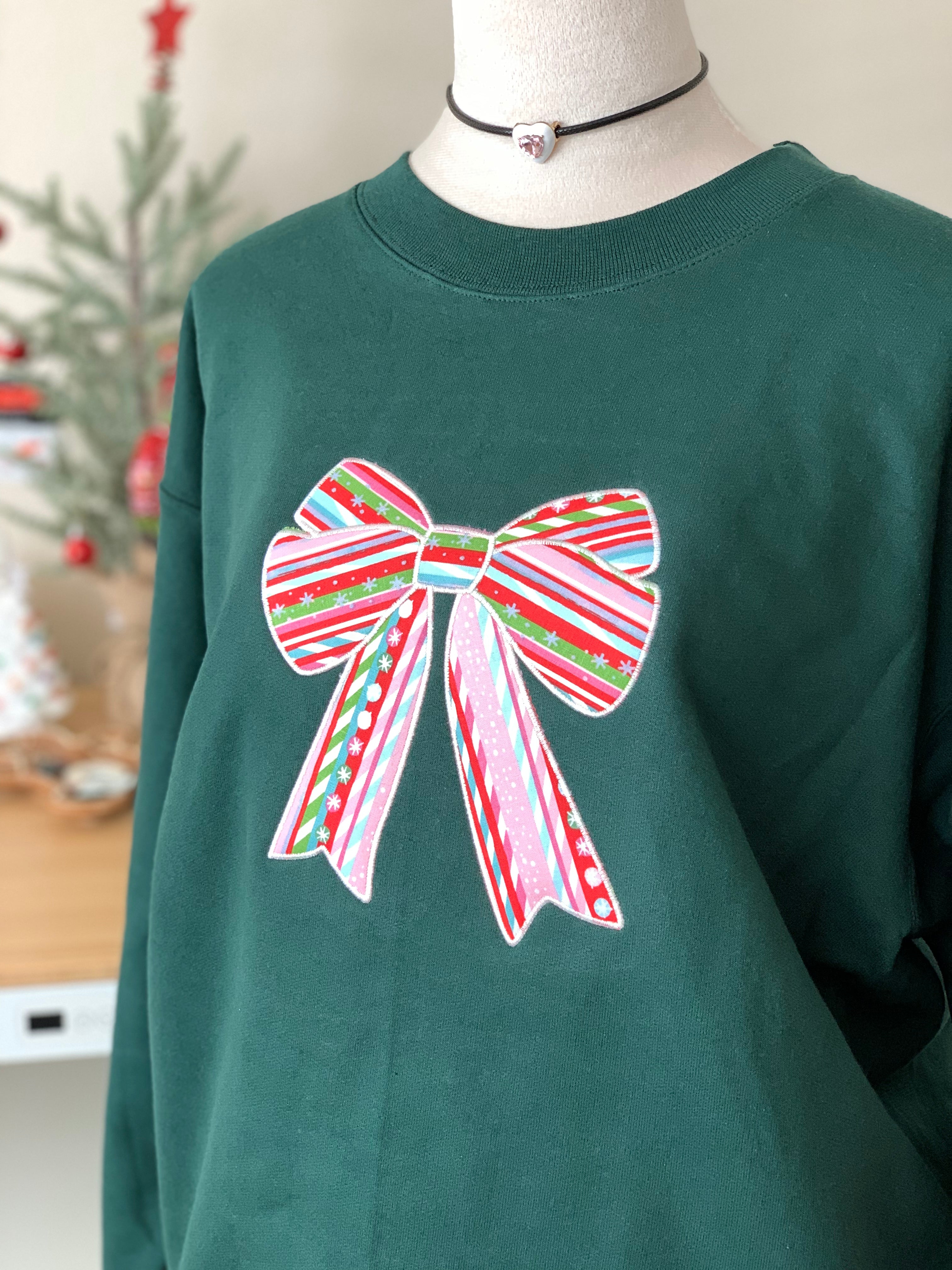 Side angle of green candy-cane bow sweatshirt near mini Christmas tree