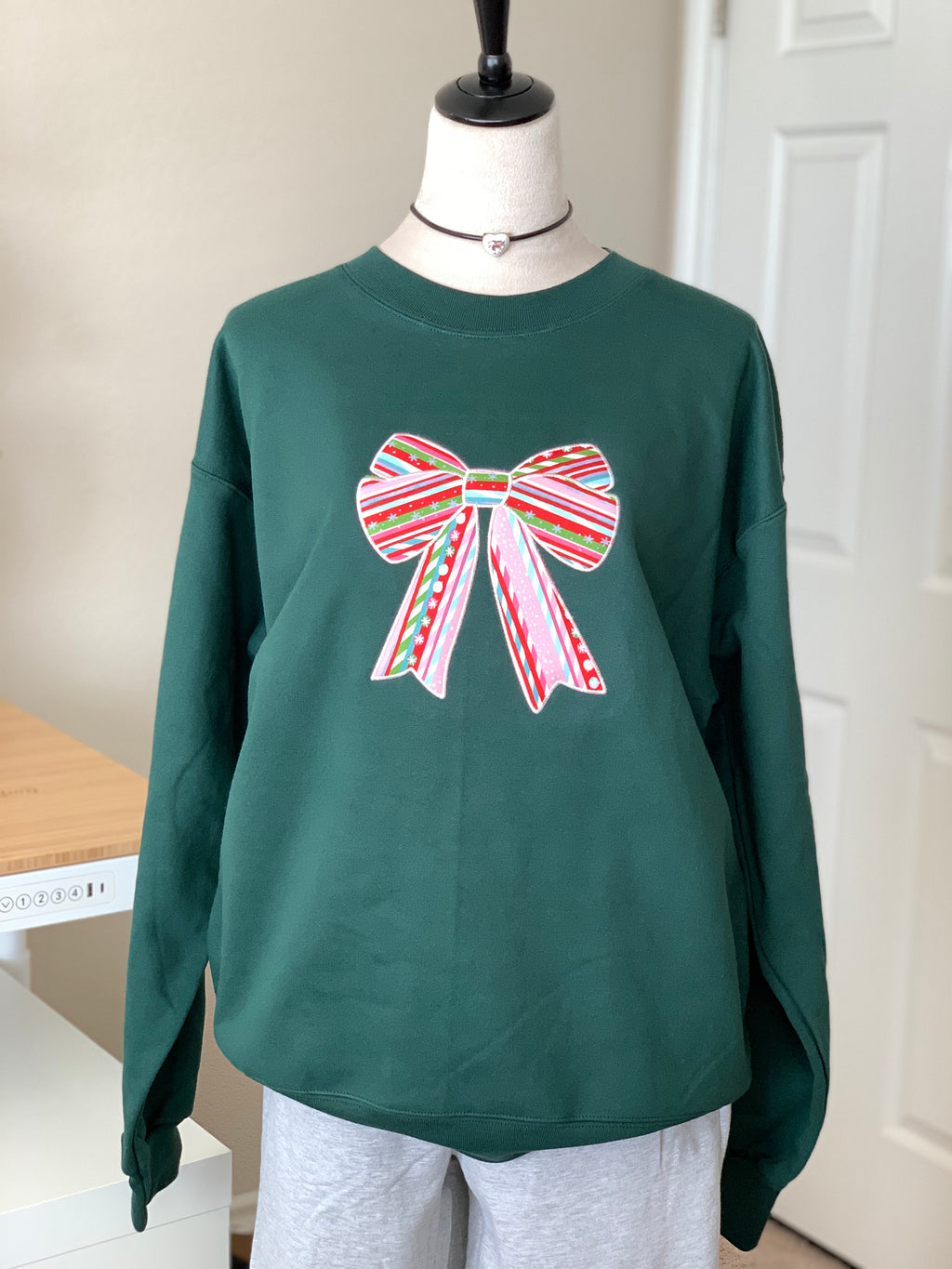 Forest green crewneck with colorful candy-cane bow, holiday vibe