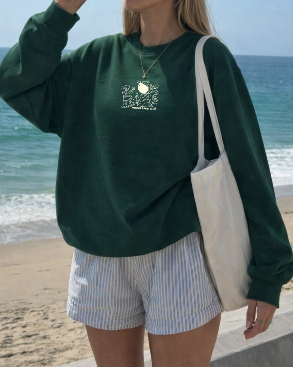 Woman wearing oversized forest green crewneck sweatshirt with small “Good Things Take Time” graphic, cozy affirmation sweatshirt styled for casual beach outfit.