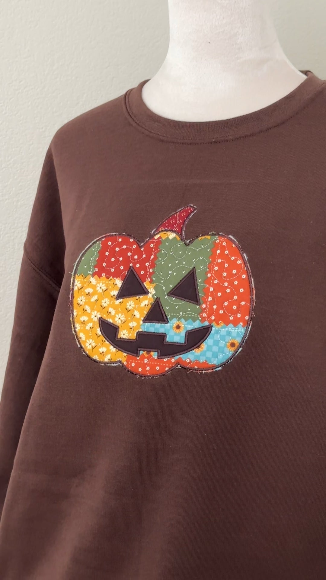 Close-up of brown sweatshirt with colorful patchwork jack-o’-lantern pumpkin applique stitched on the front.
